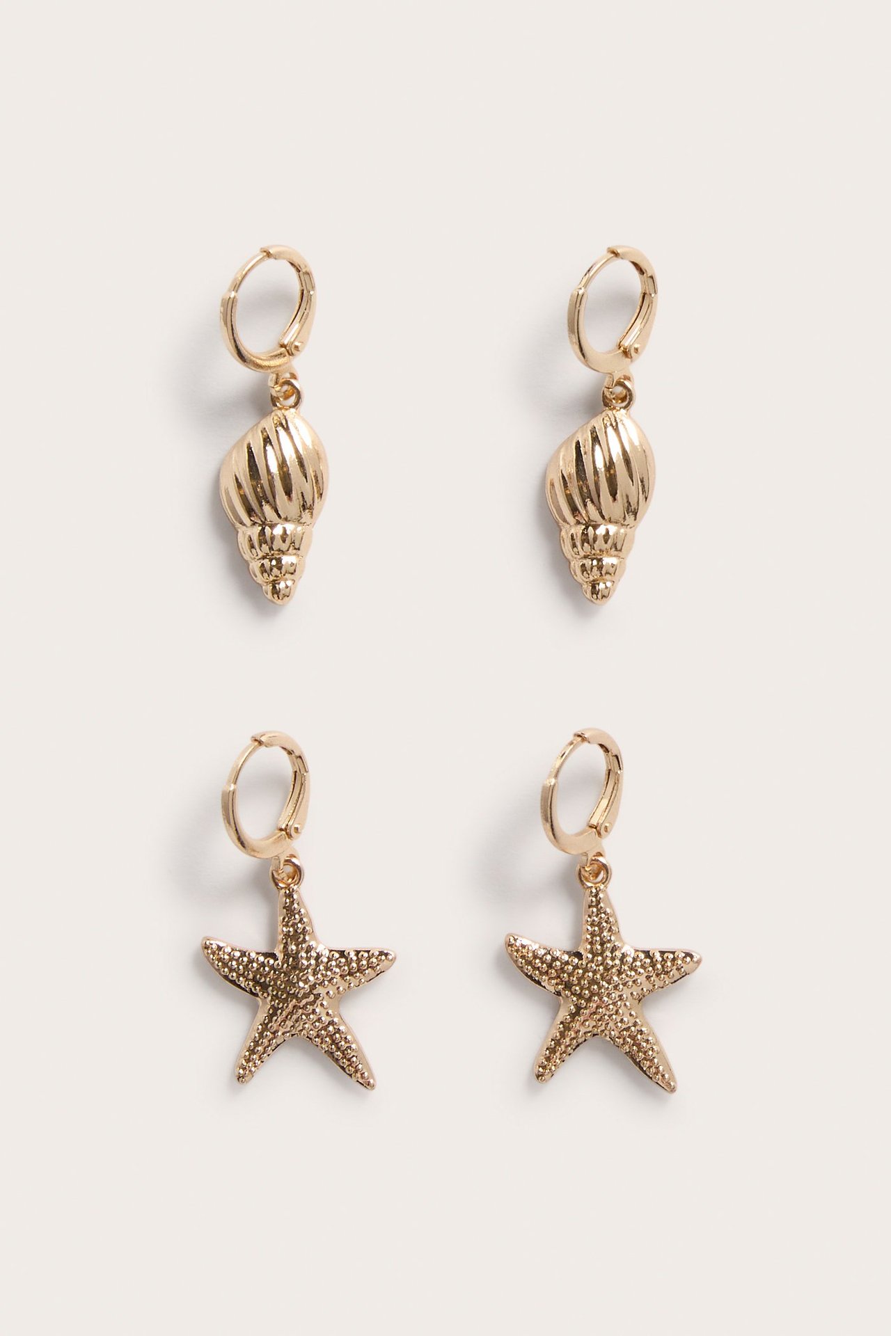 Lähikuva 2-pakkauksesta kultaisia metallirenkaita, joissa on simpukka- ja meritähtiriipukset.