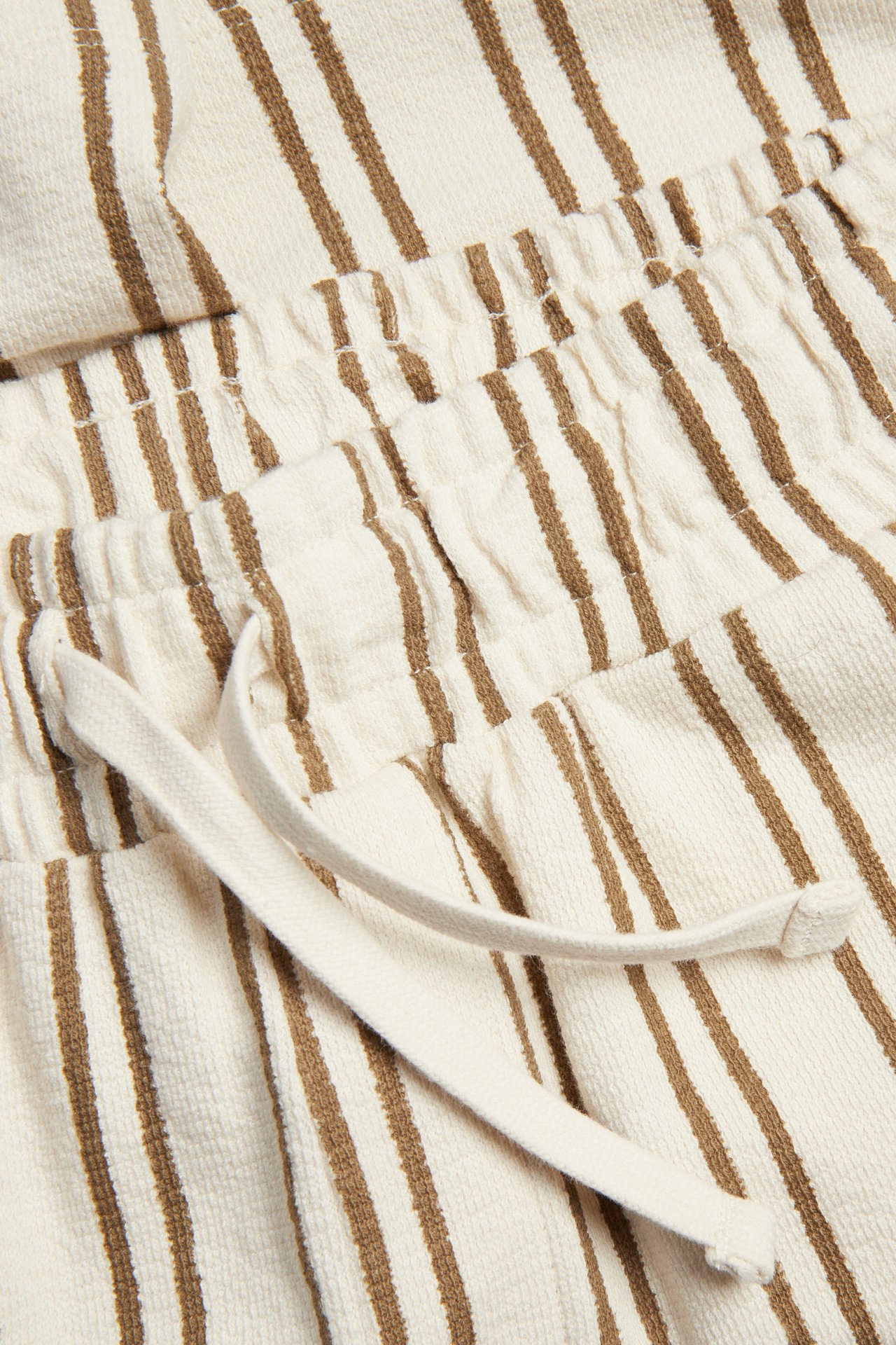 Lähikuva raidoitetuista ruskea-valkoisista jersey-shortseista, joissa säädettävä, joustava vyötärönyöri.