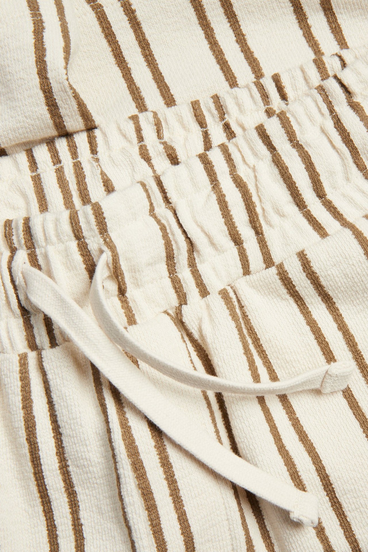 Zbliżenie na paski brązowo-kremowe szorty dżersejowe z elastycznym, regulowanym sznurkiem w pasie.