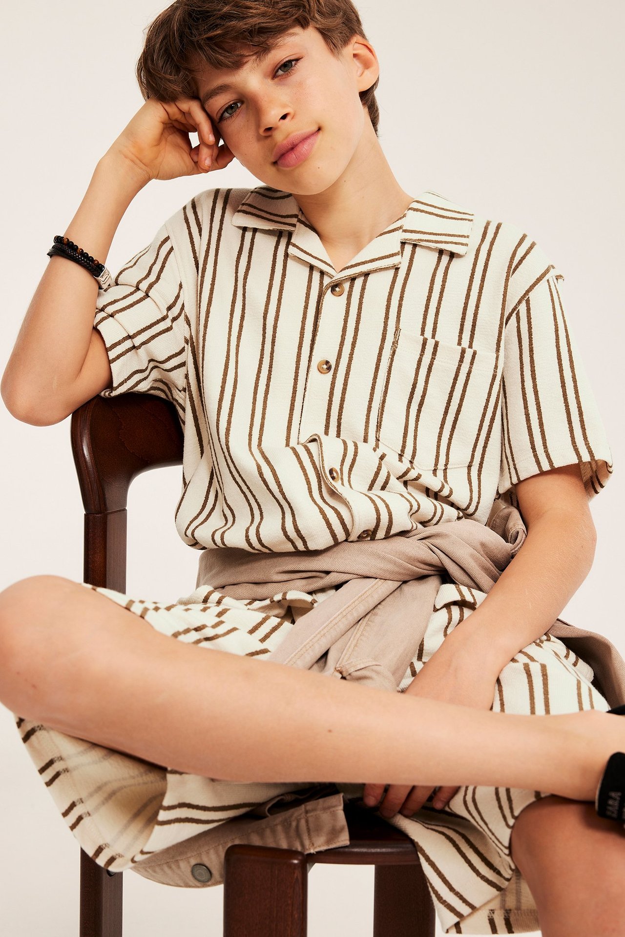 Frontvy av ett barn i off-vit, brunrandig bomullsjersey skjorta och matchande shorts-set.