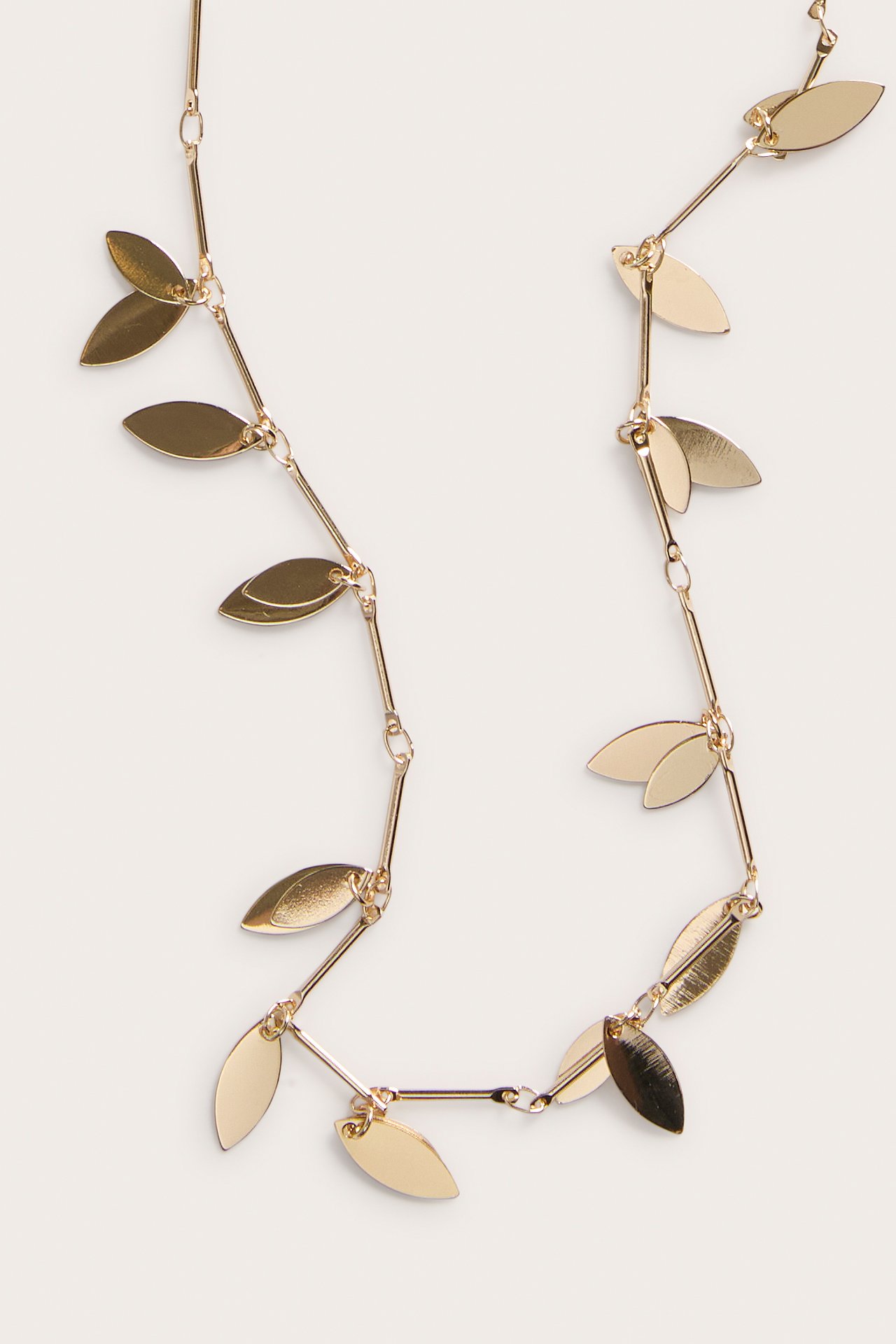 Närbild av ett guldfärgat metallhalsband med små blanka, bladformade detaljer länkade ihop.