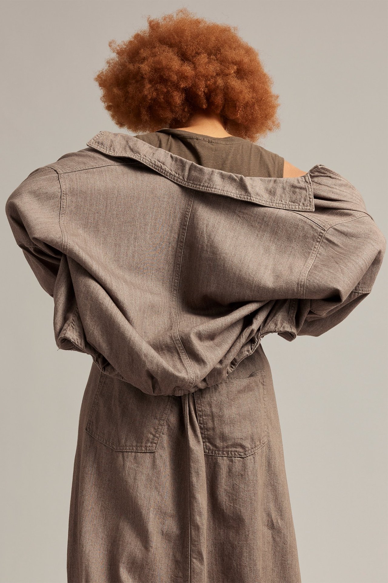 Nainen selin, yllään melerattu ruskea denim-blouson-takki, tumma t-paita ja yhteensopiva hame.