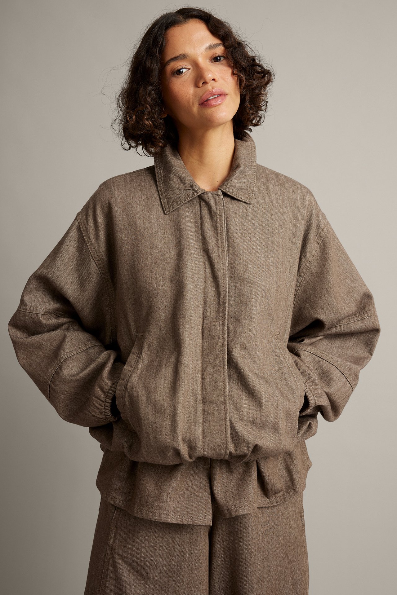 Framifrån bild av kvinnlig modell med brun avslappnad krage jacka och matchande byxor.