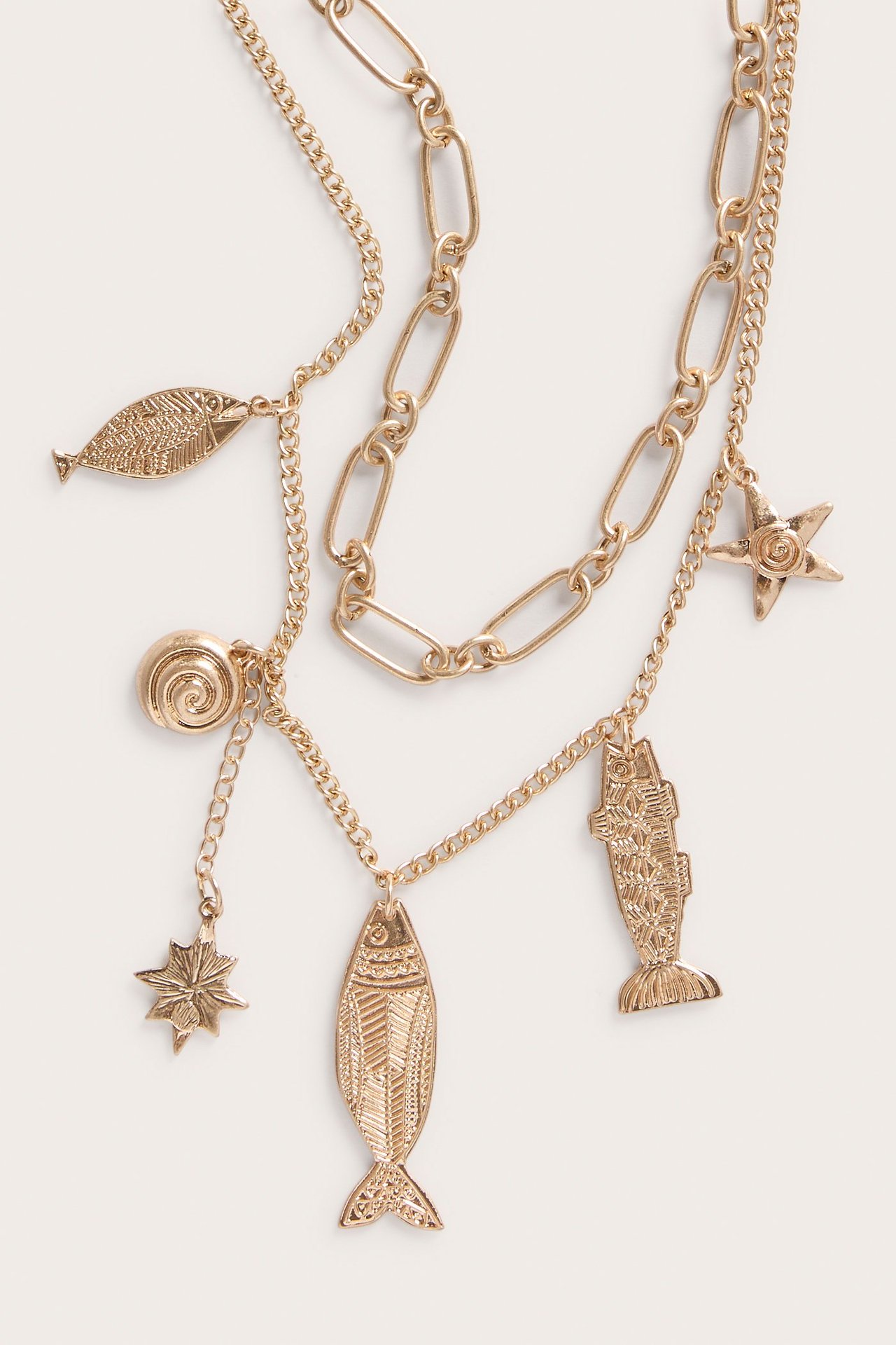 Lähikuva kultaisesta monikerroksisesta kaulakorusta, jossa merihenkisiä riipuksia: kaloja, simpukka ja meritähtiä.