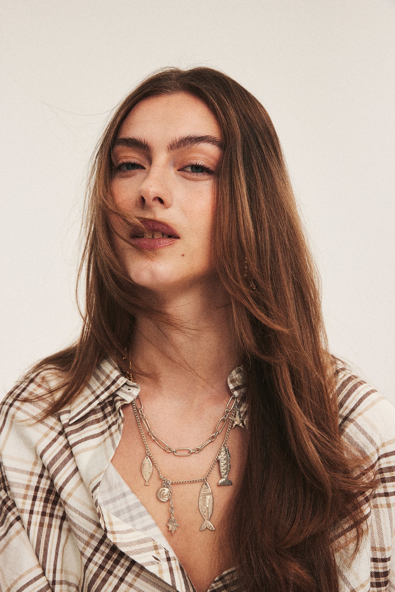 Närbild av kvinna i beige rutig skjorta som bär silverfärgat halsband med marina berlocker.