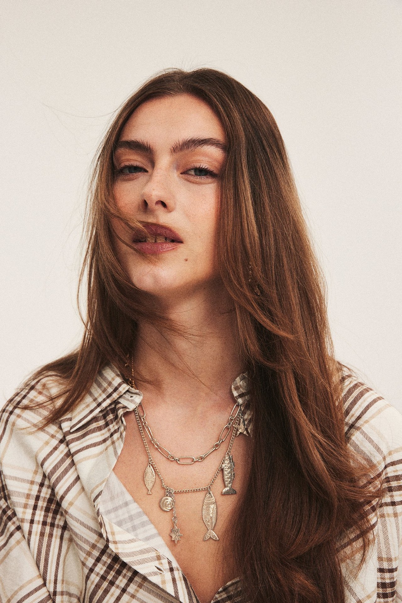 Närbild av kvinna i beige rutig skjorta som bär silverfärgat halsband med marina berlocker.