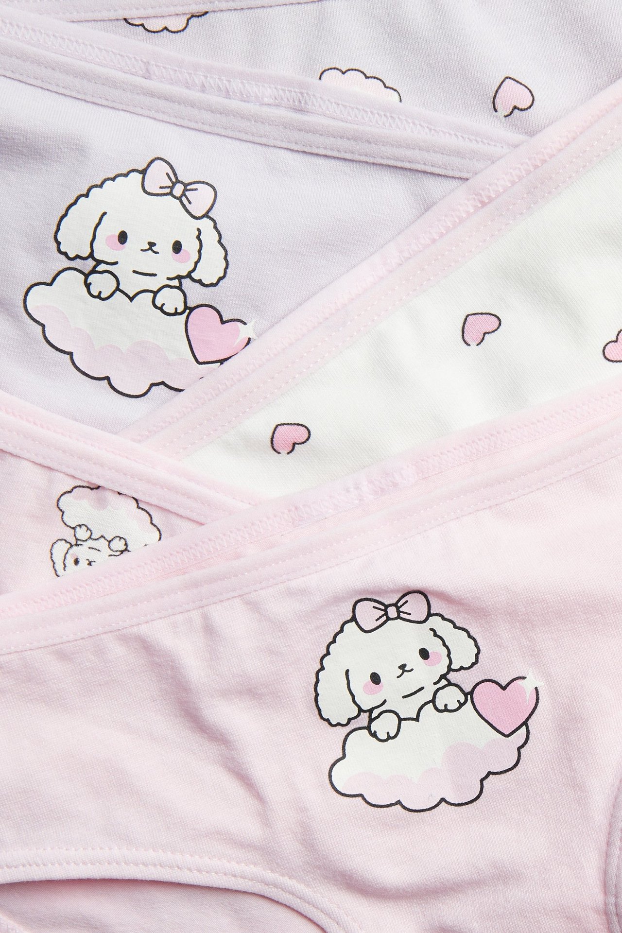 Zbliżenie na trzy dziecięce figi z organicznej bawełny w różu, jasnym fiolecie i bieli, z wzorem psa i serc.