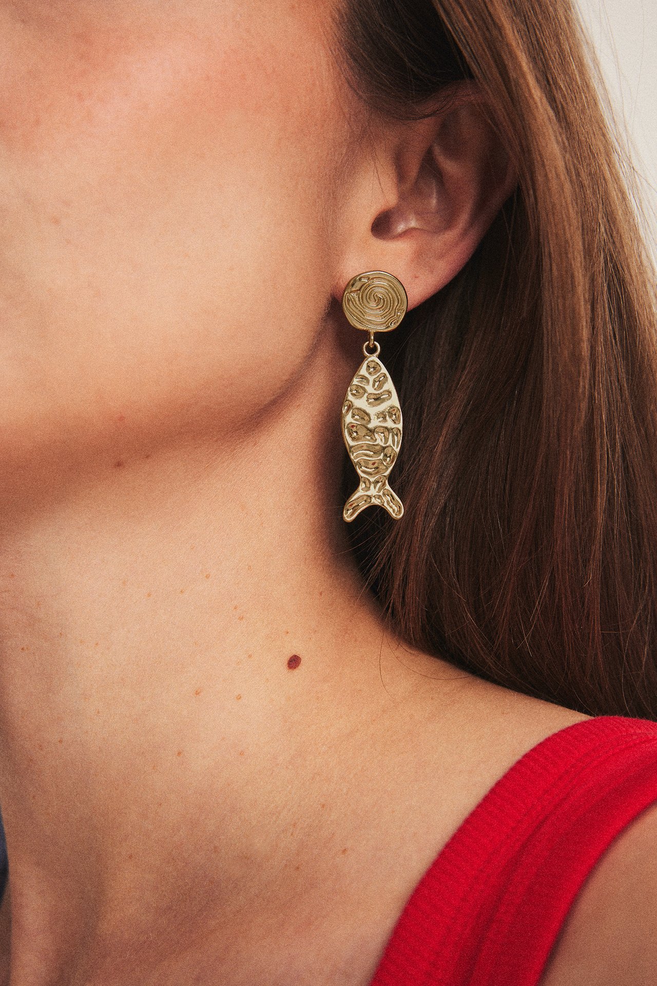 Lähikuva naisesta, jolla on kultainen kalankuvioinen korvakoru, jossa on kuvioitu pinta ja spiraalipää.