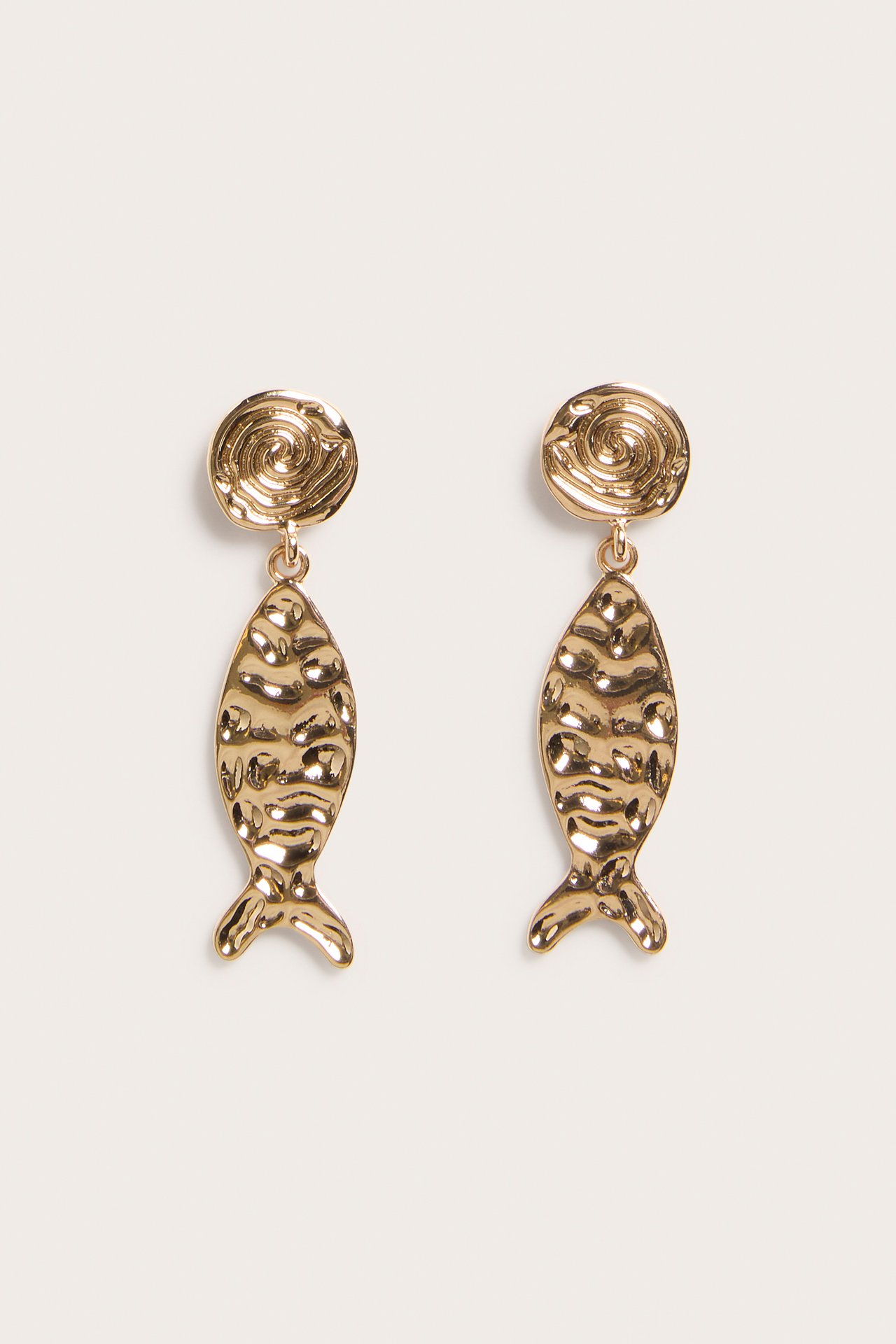 Närbild framifrån av två guldfärgade metallörhängen, med spiralformad knopp och hamrad fiskformad berlock.