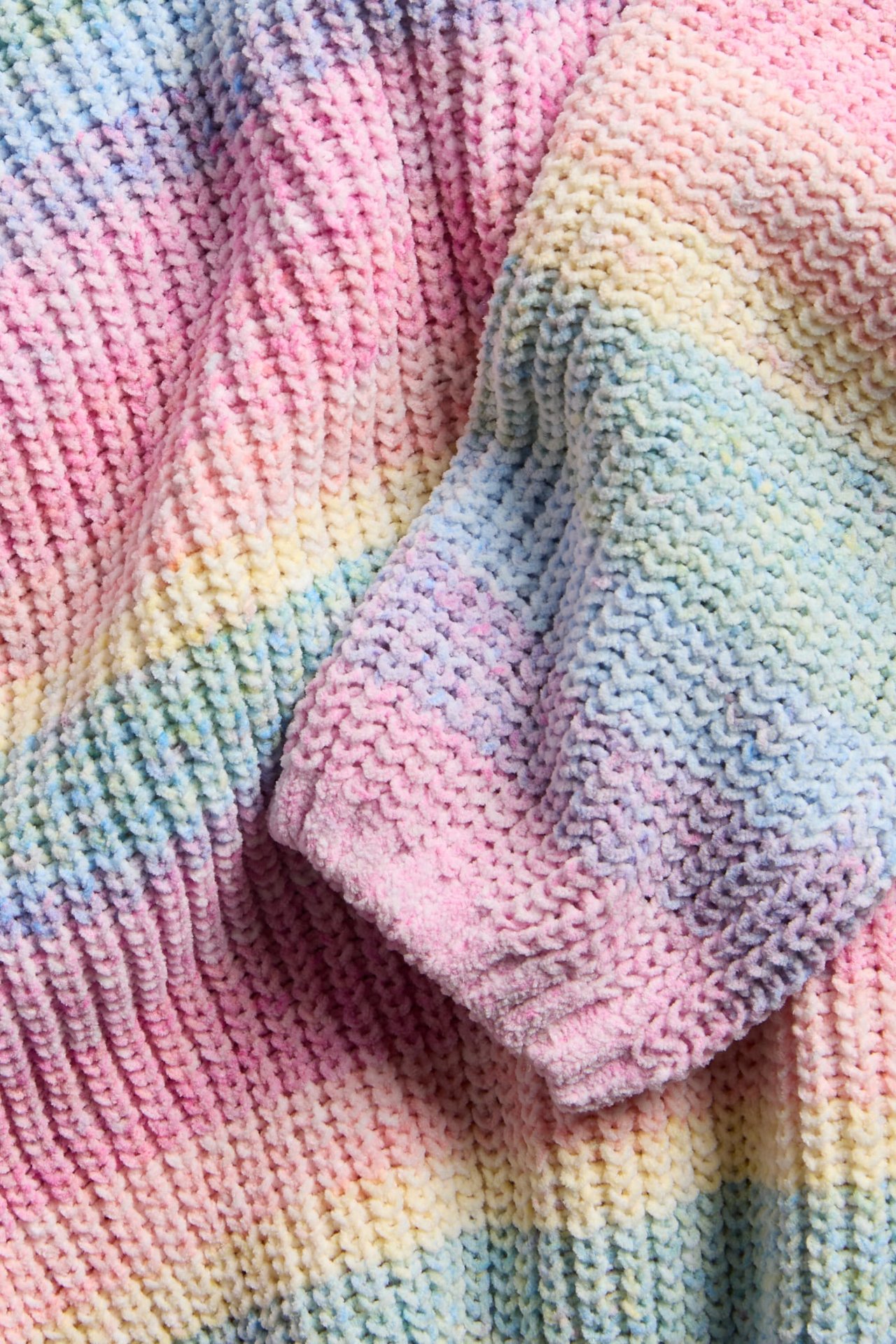 Närbild av en pastellfärgad regnbågsrandig tjockstickad tröja med mjuk textur.