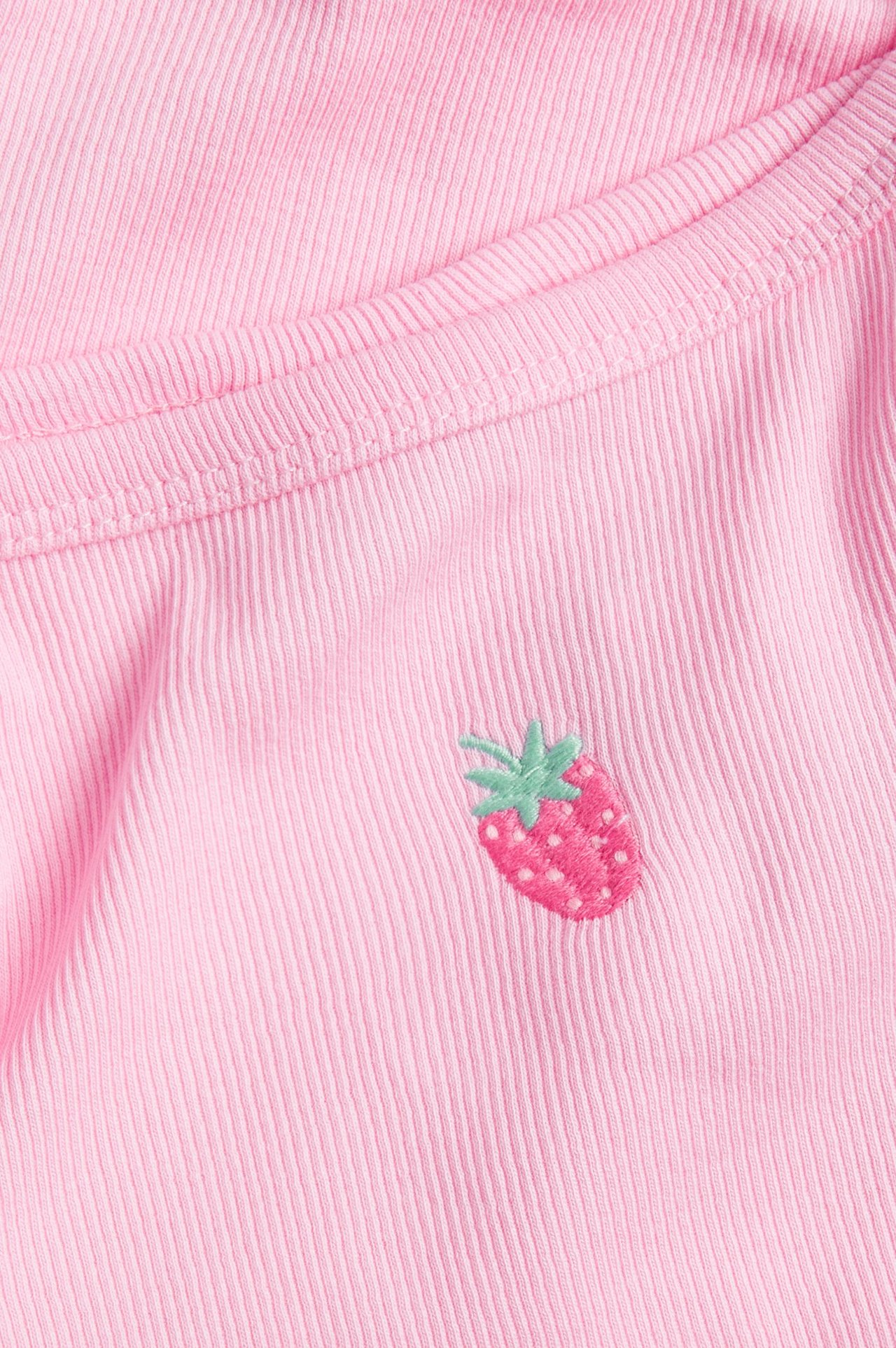 Lähikuva vaaleanpunaisesta ribbipaidasta, jossa on pieni kirjailtu mansikka edessä.