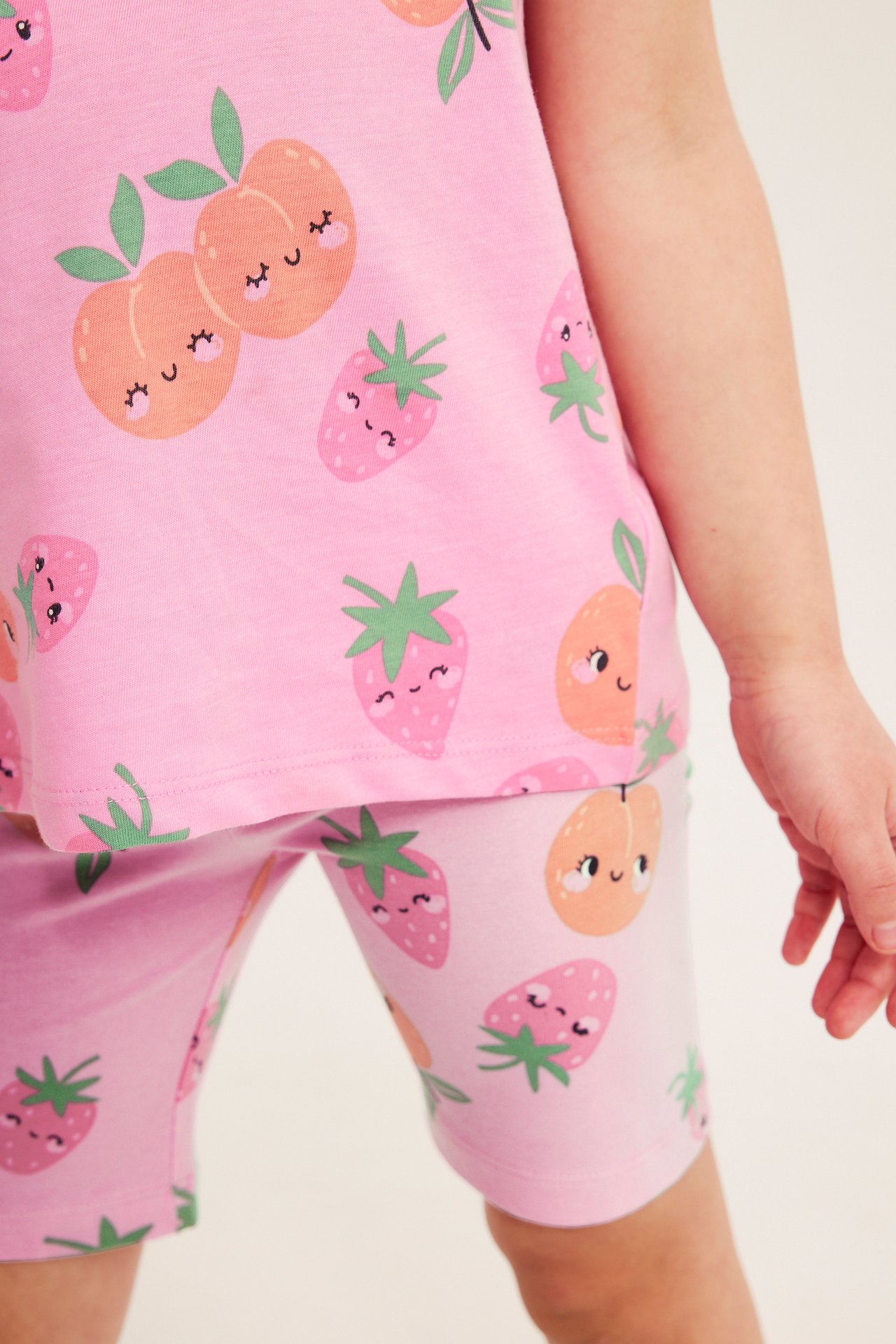 Lähikuva lapsesta, jolla on vaaleanpunaiset puuvillaiset pyöräilyhousut iloisella hedelmäkuviolla ja yhteensopiva toppi.