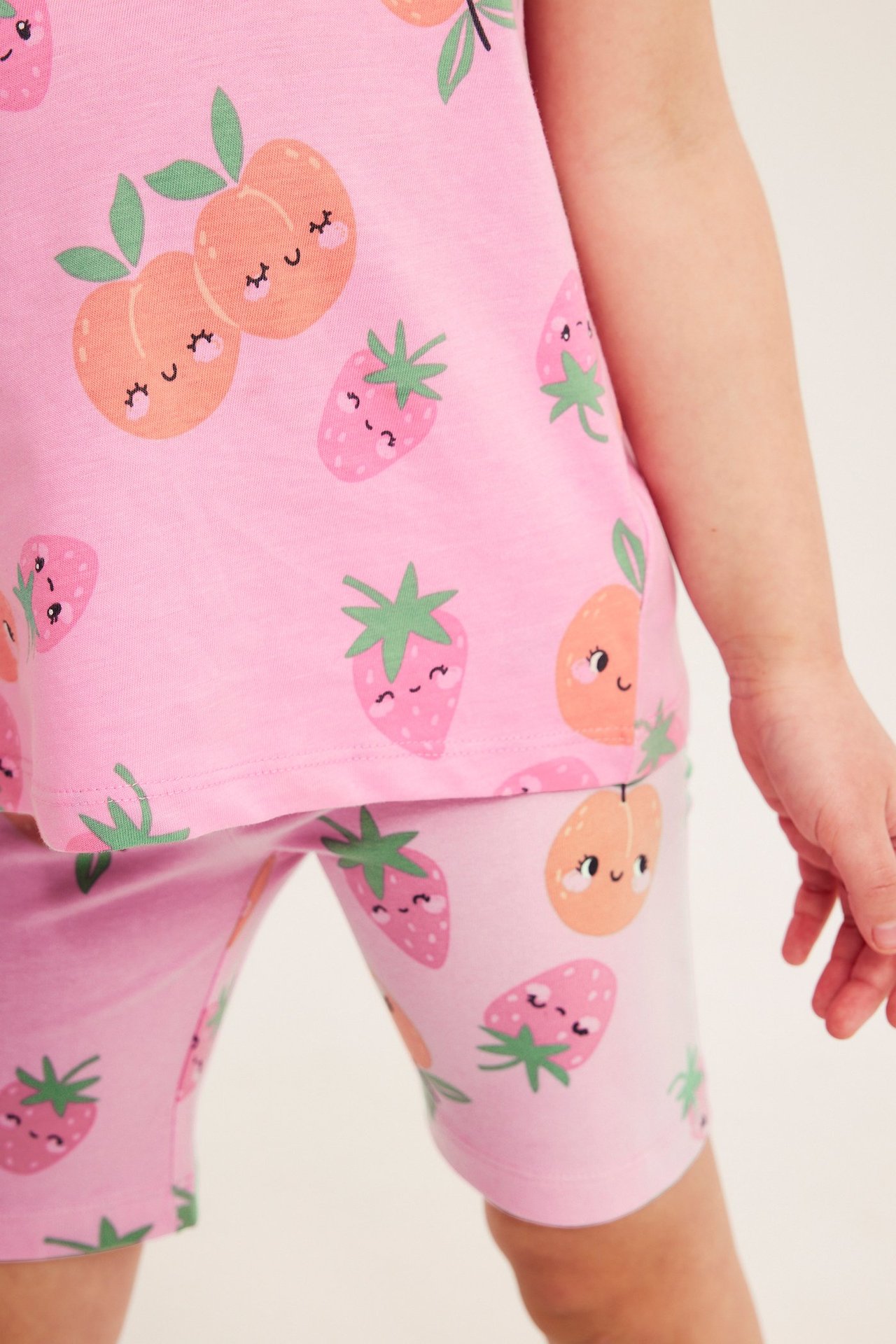 Lähikuva lapsesta, jolla on vaaleanpunaiset puuvillaiset pyöräilyhousut iloisella hedelmäkuviolla ja yhteensopiva toppi.