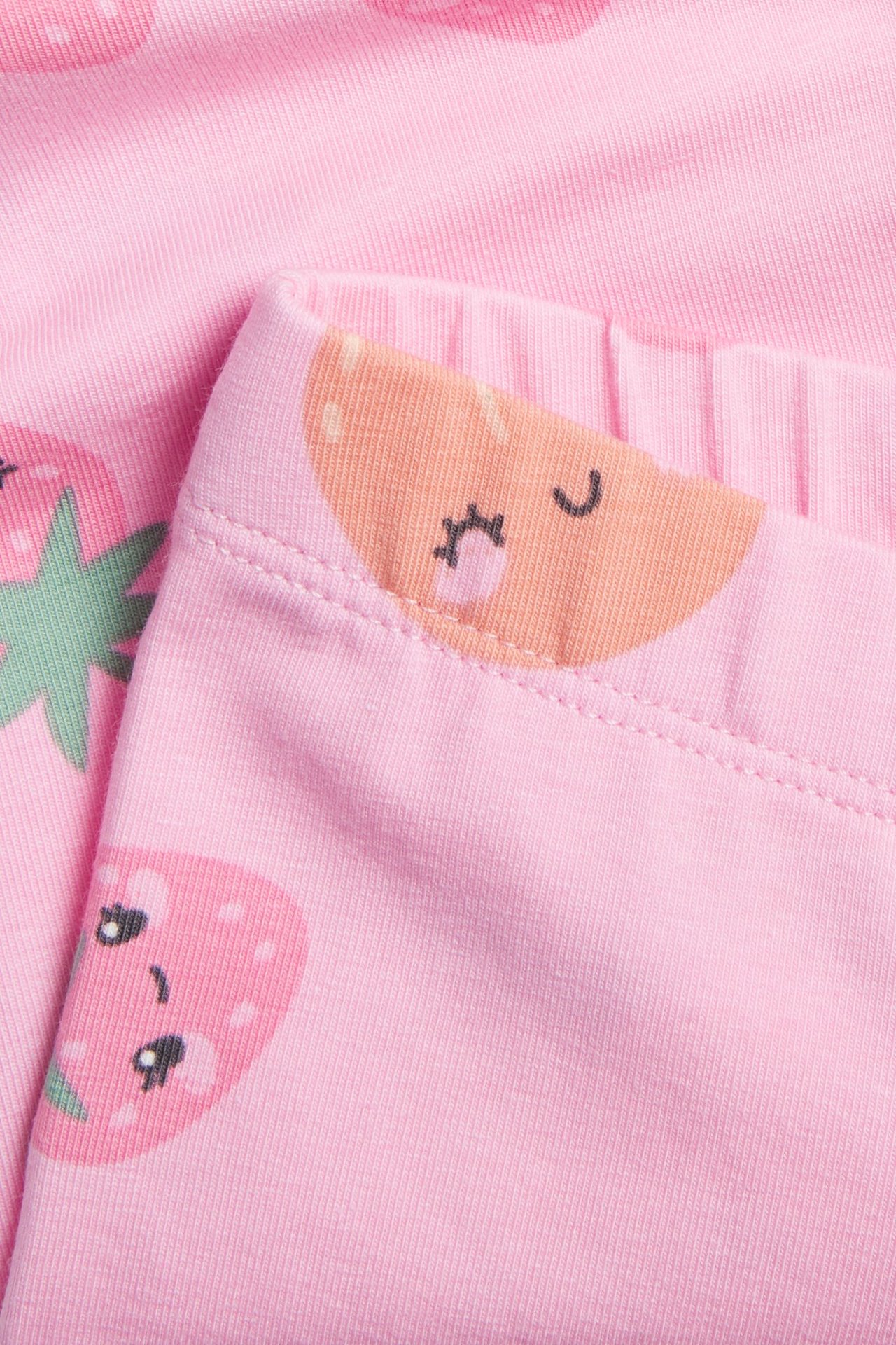 Lähikuva vaaleanpunaisista puuvillaisista pyöräilyshortseista joustavalla vyötäröllä ja söpöllä hedelmäkuviolla.