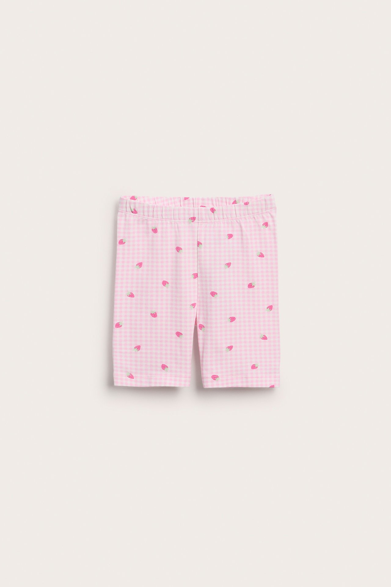 Edestä, lasten vaaleanpuna-valkoinen ruudullinen puuvillainen pyöräilyshortsi joustavalla vyötäröllä ja mansikkakuviolla.