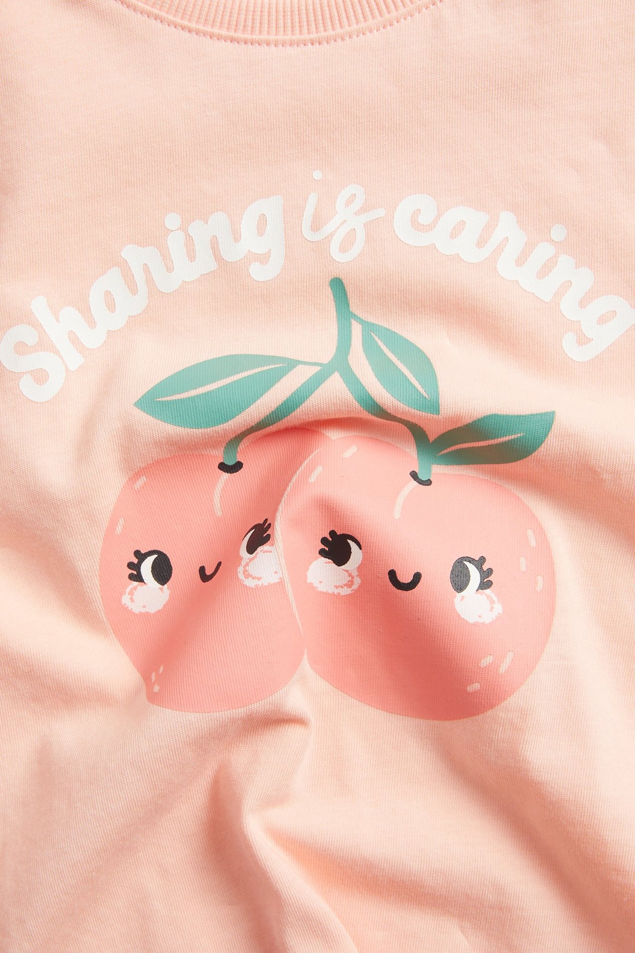 Zbliżenie z przodu na koralowy bawełniany T-shirt dziecięcy z nadrukiem brzoskwiń i napisem.