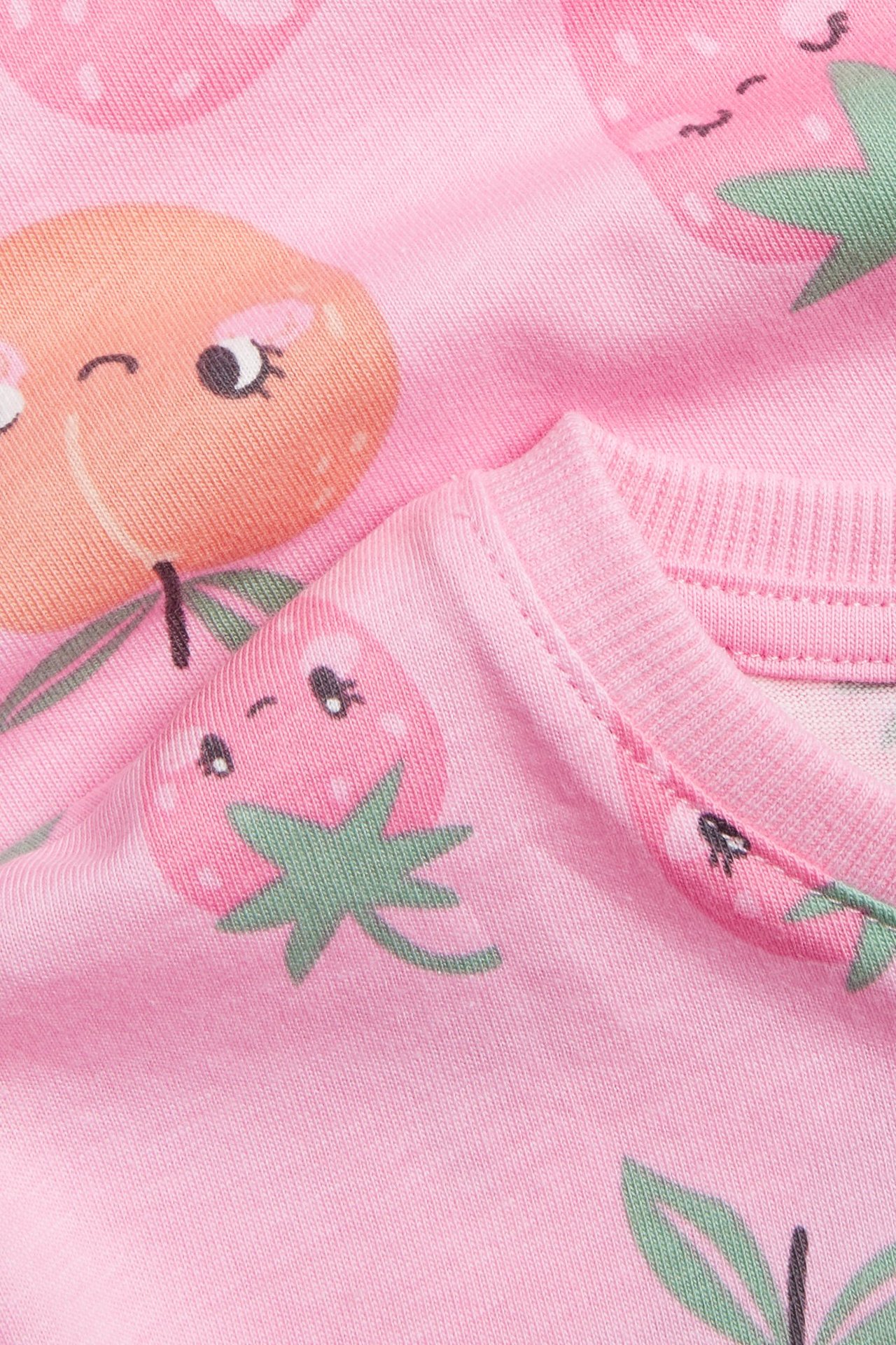 Zbliżenie: różowy bawełniany T-shirt dziecięcy z wzorem truskawek i brzoskwiń, z okrągłym dekoltem.