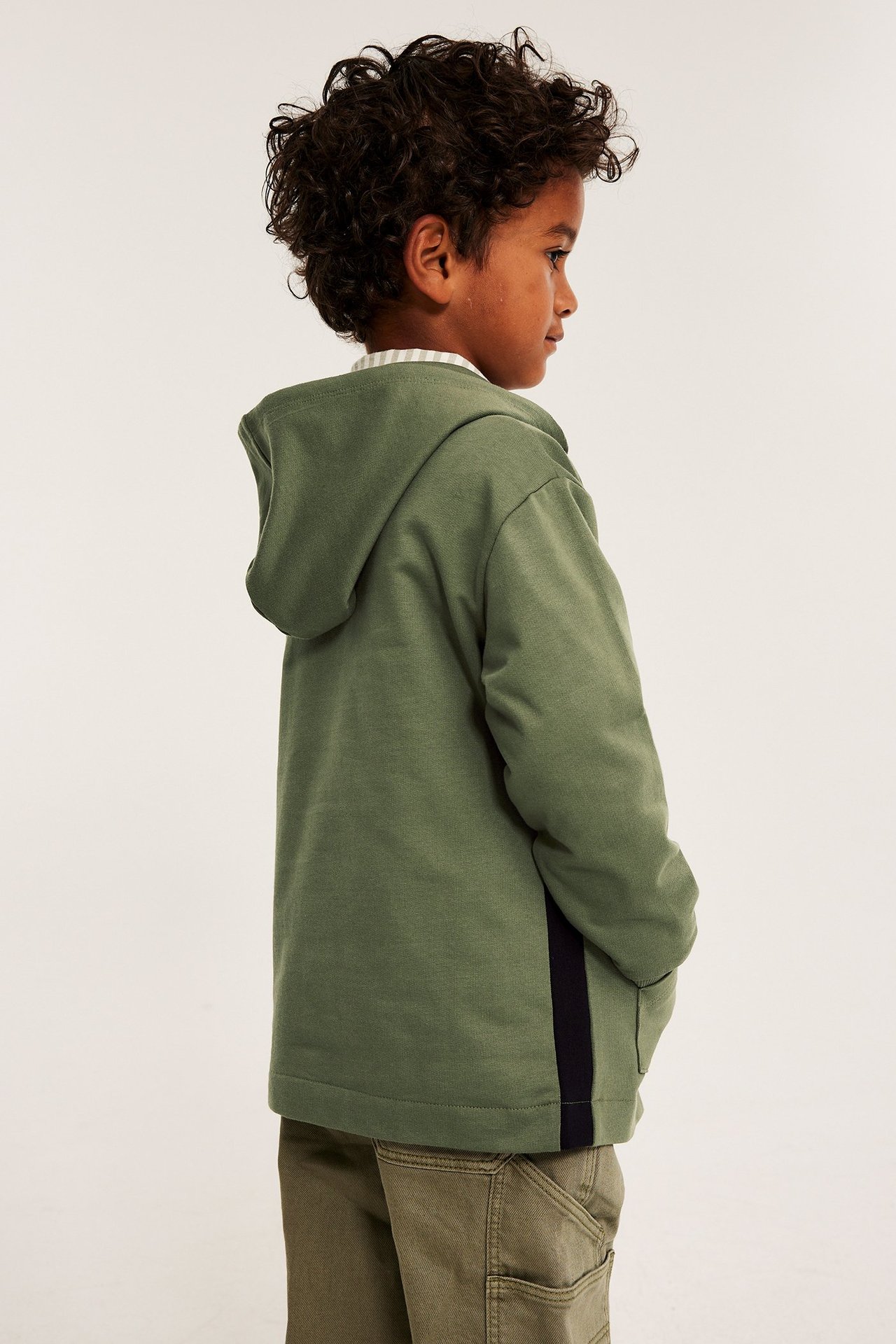 Widok z boku: Dziecko w ciemnozielonej bawełnianej bluzie z kapturem z ciemnym panelem, koszuli i oliwkowych spodniach.