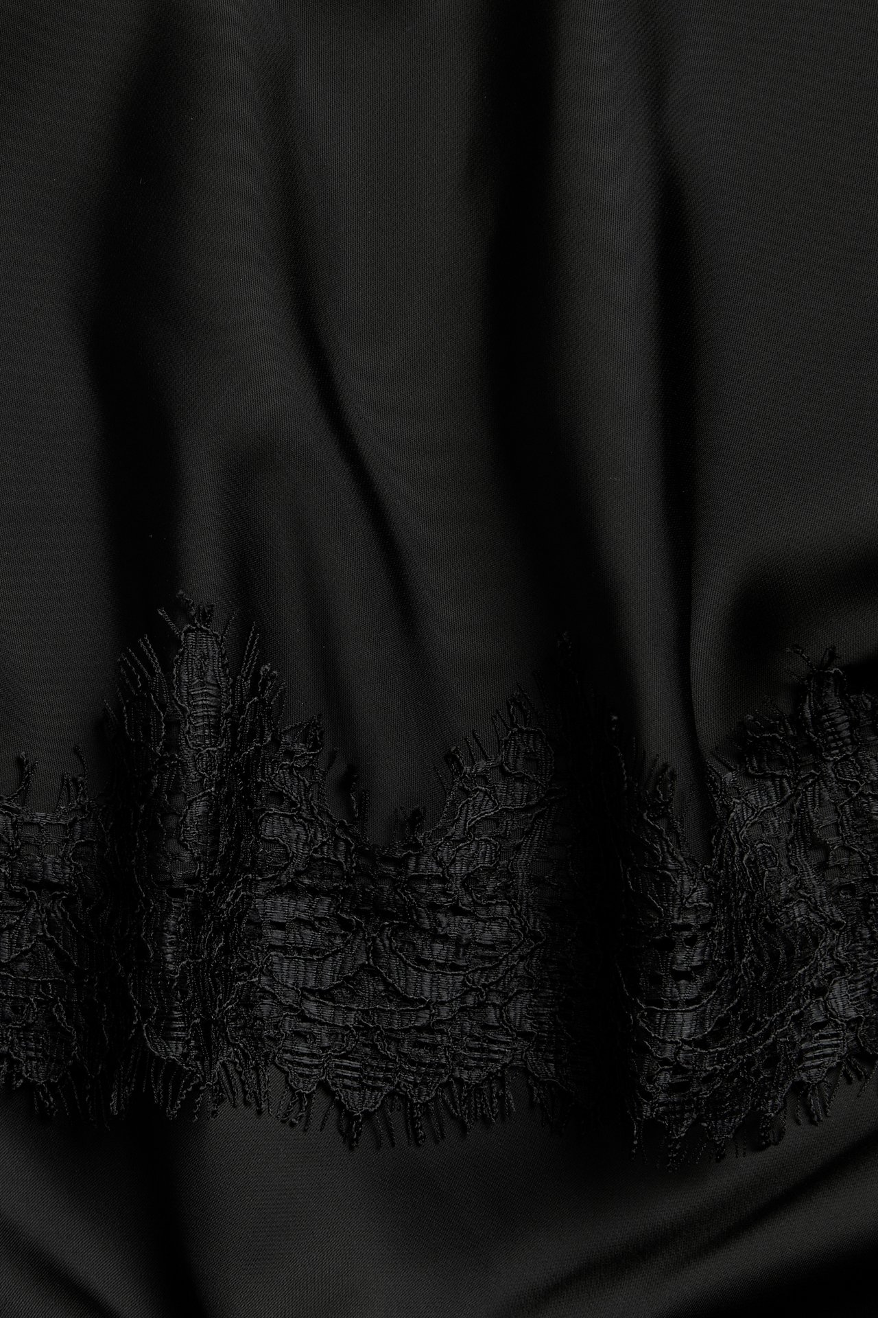 Nærbilde av et svart satengskjørt med detaljert blondekant langs bunnen.