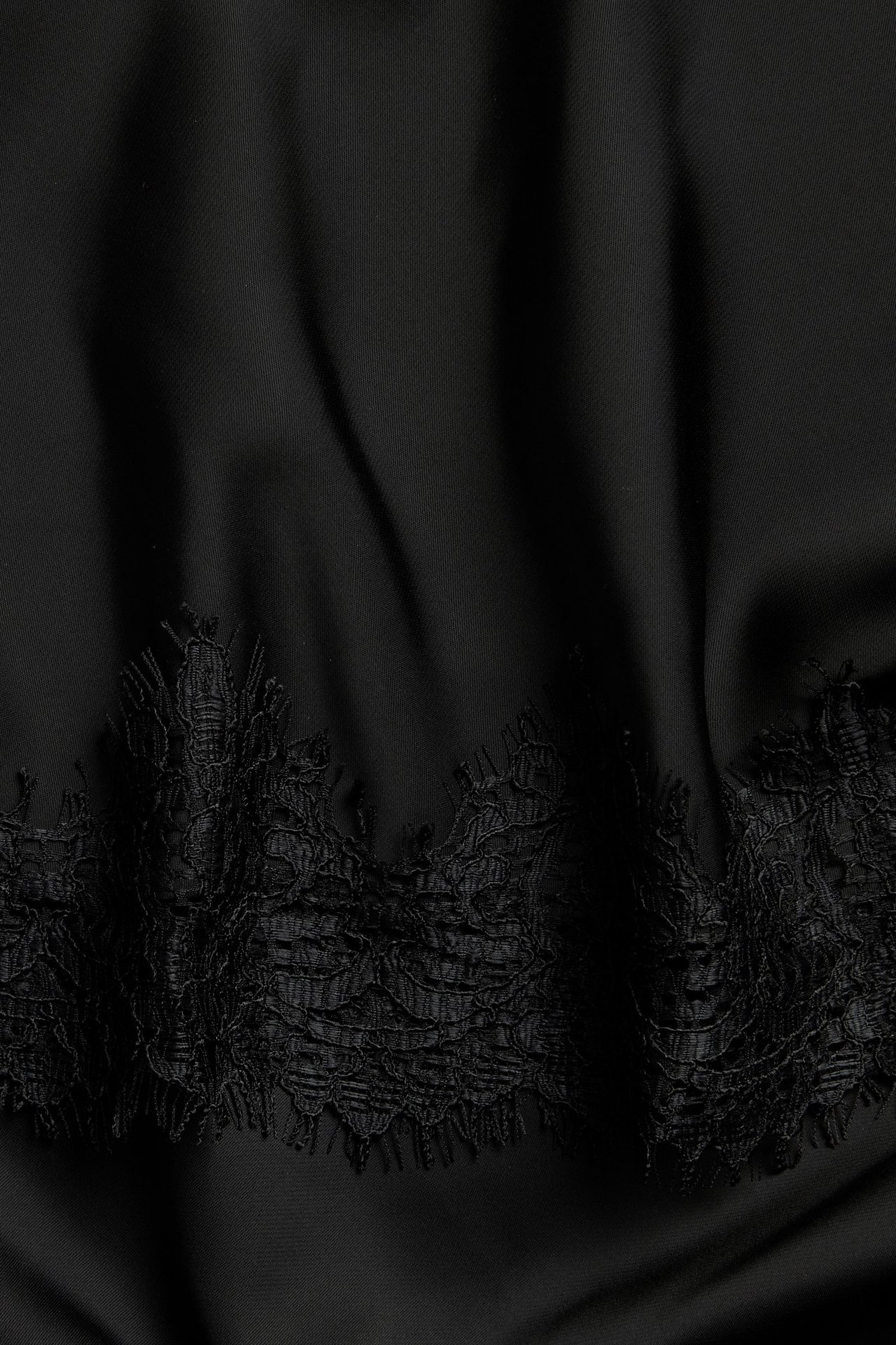 Zbliżenie czarnej satynowej spódnicy z ozdobnym koronkowym wykończeniem na dole.