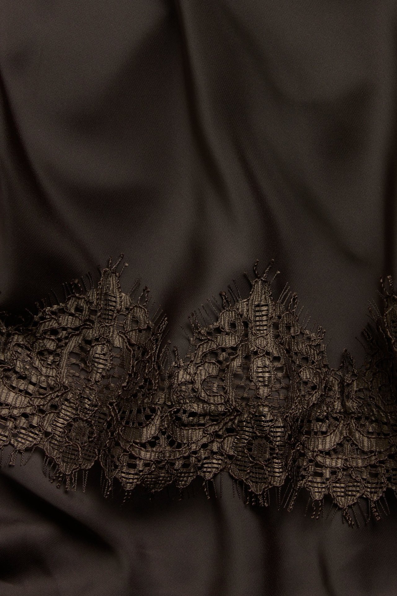 Närbild på en brun satinkjol med detaljerad mörk spetskant längs nederkanten.