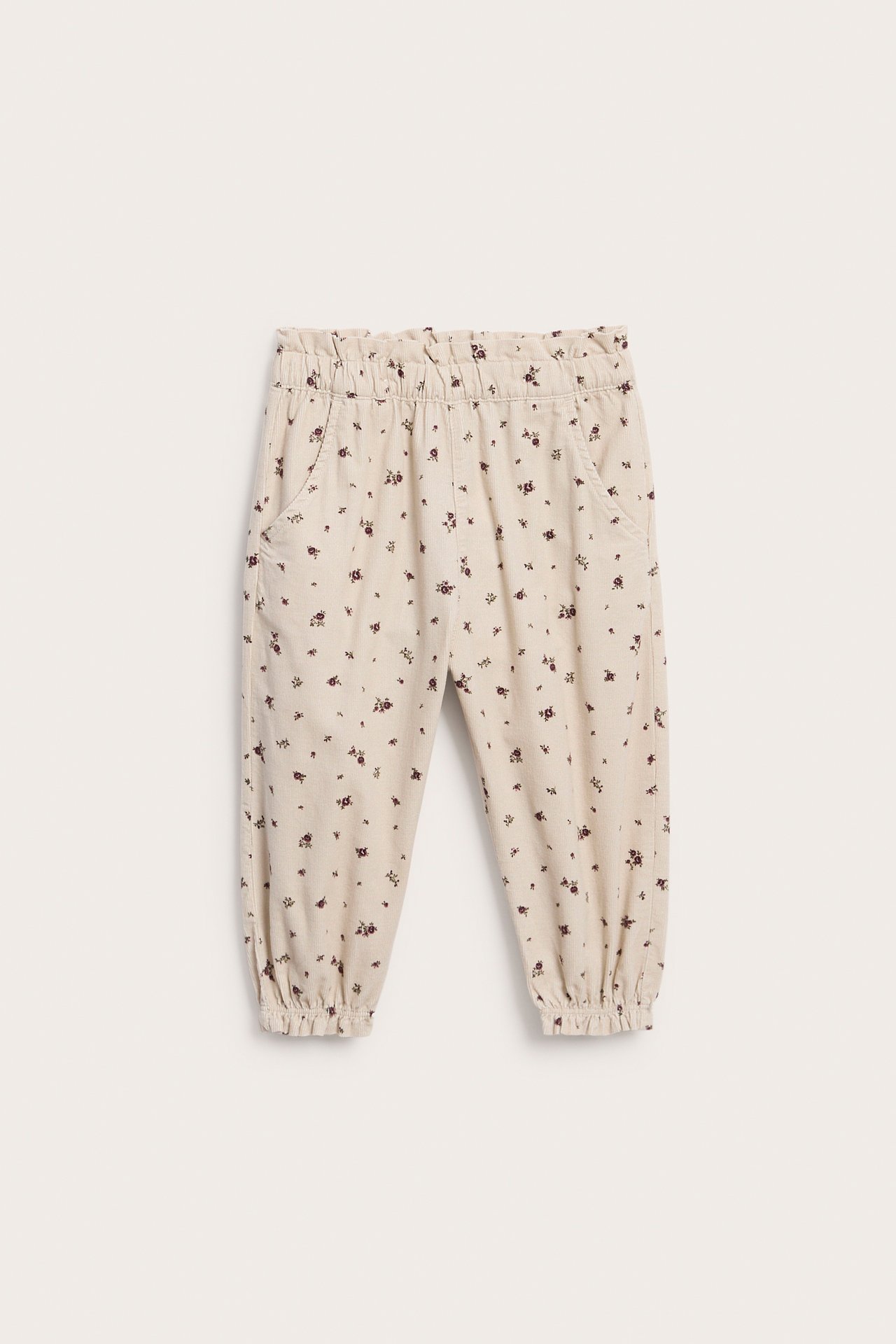 Frontvisning av beige blomstrete joggebukse med strikk i midjen og nederst for barn.