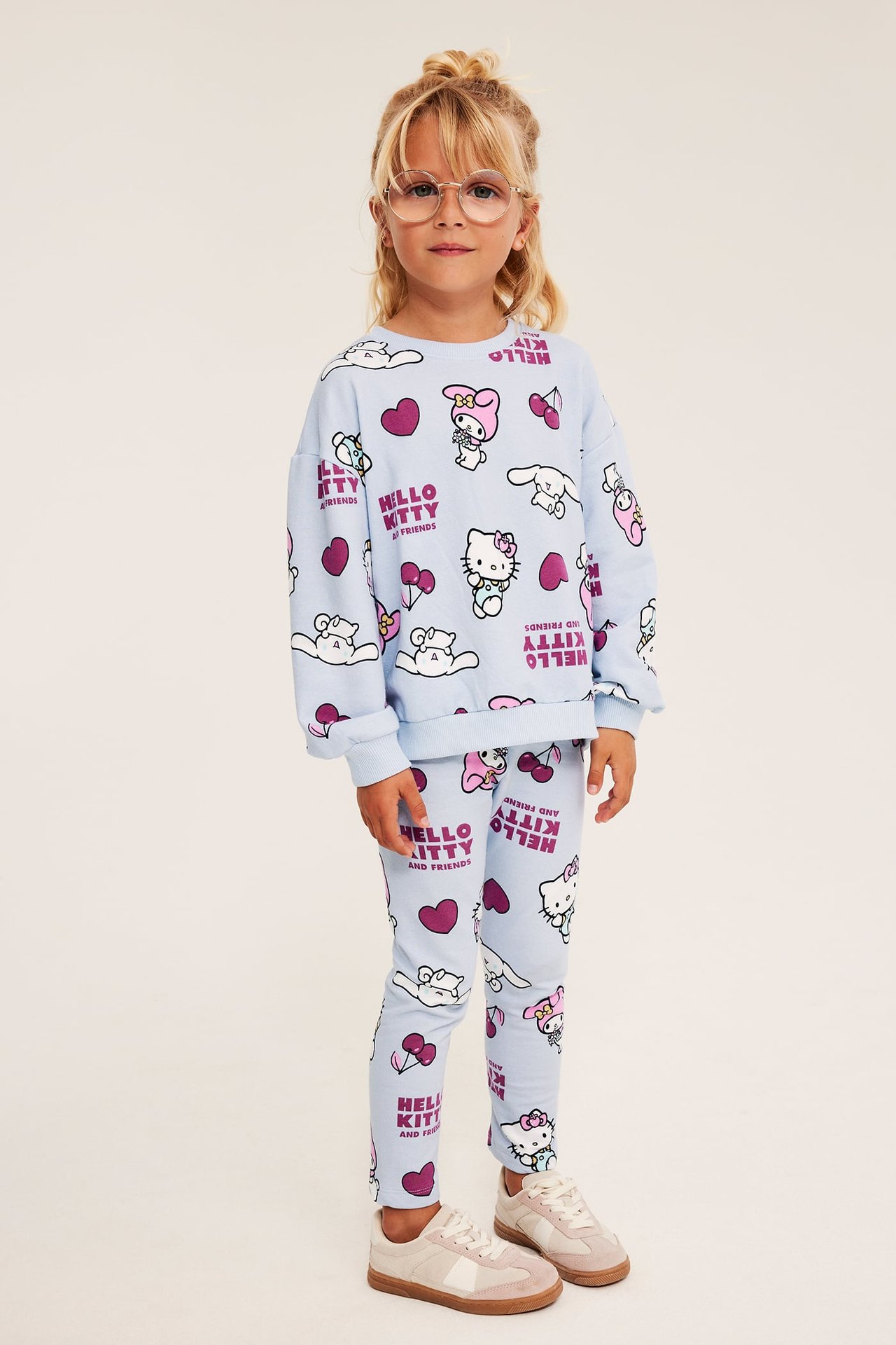 Forfra, et barn i en lyseblå Hello Kitty and Friends-mønstret treningsdress med genser og leggings.