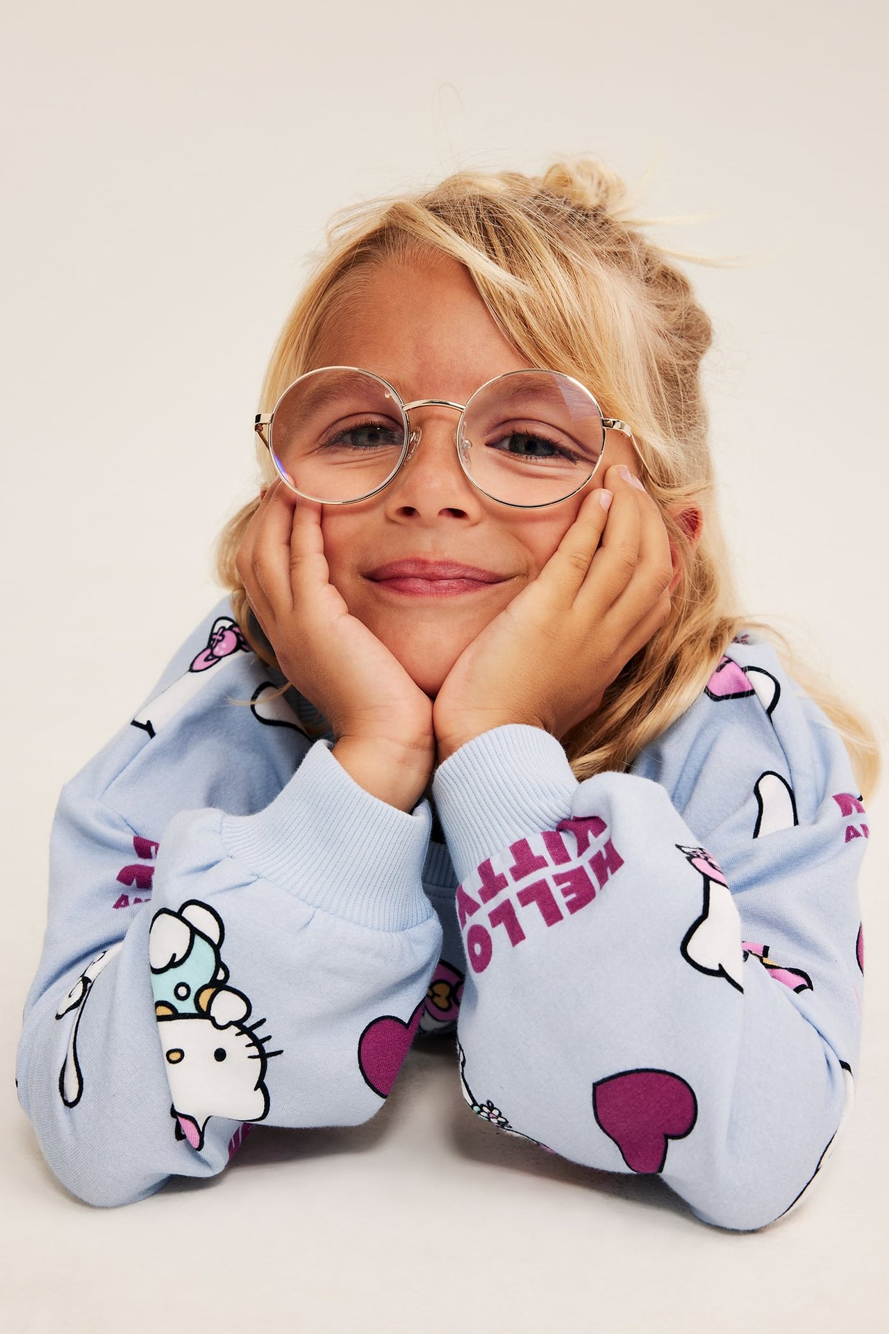 Przodem, dziecko w okrągłych okularach i jasnoniebieskiej bluzie z nadrukiem Hello Kitty.