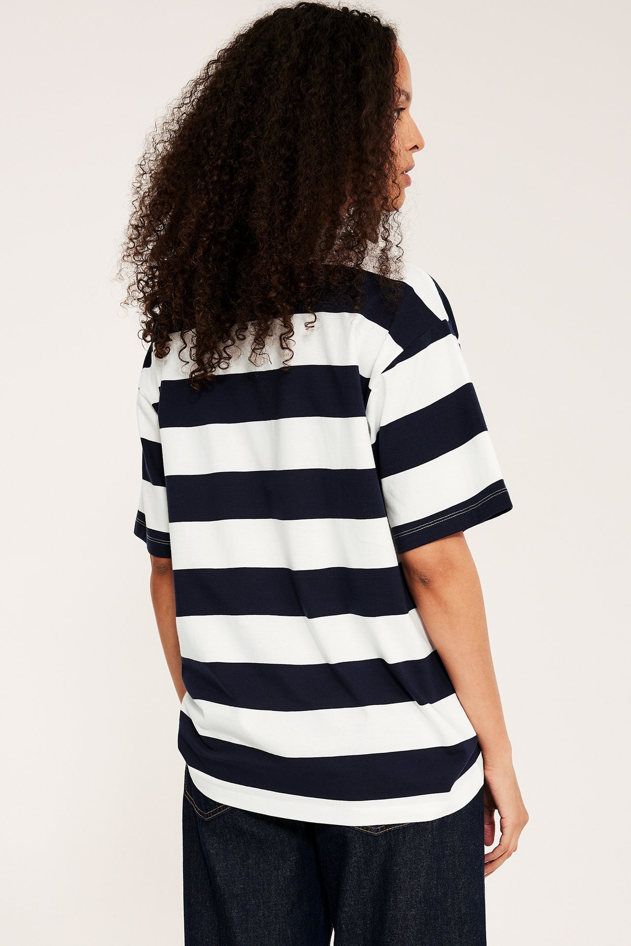 Nainen takaapäin, oversized tummansininen-valkoinen raidallinen puuvilla T-paita ja tummat farkut.