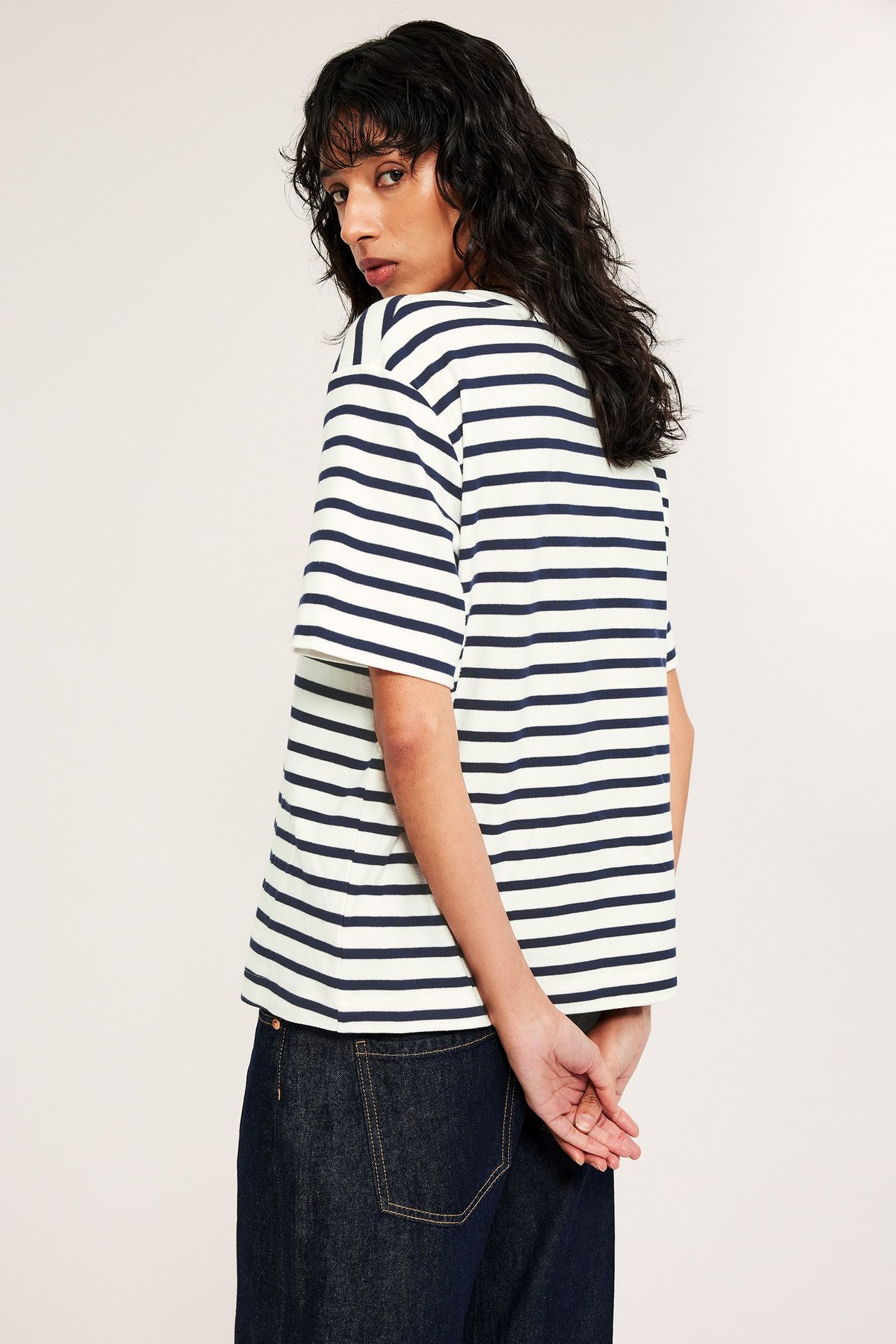 Nainen selkäpuolelta oversized valkoisessa ja tummansinisessä raidallisessa puuvilla-T-paidassa ja tummansinisissä farkuissa.