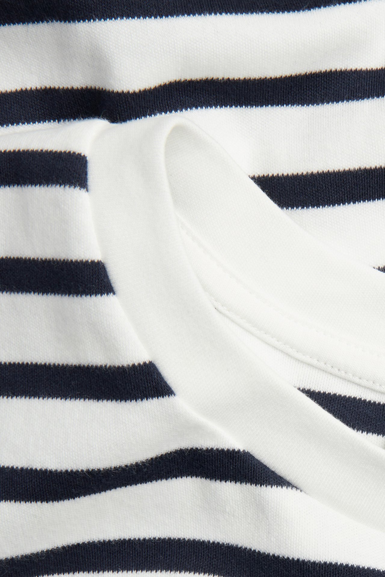 Lähikuva tummansinisestä ja valkoisesta raidallisesta oversized puuvilla-t-paidasta, jossa valkoinen resoripääntie.