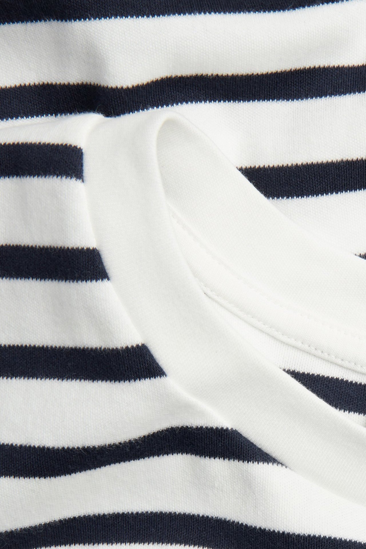 Zbliżenie na granatowo-białą, pasiastą koszulkę bawełnianą oversize z białym, prążkowanym dekoltem.