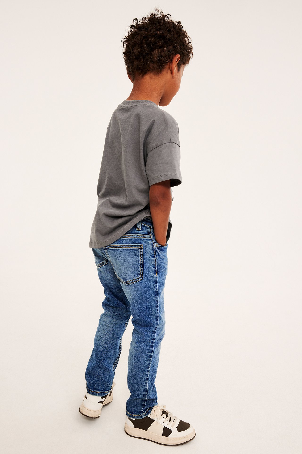 Ryggvy av ett barn i grå t-shirt, blå jeans och vita och bruna sneakers.