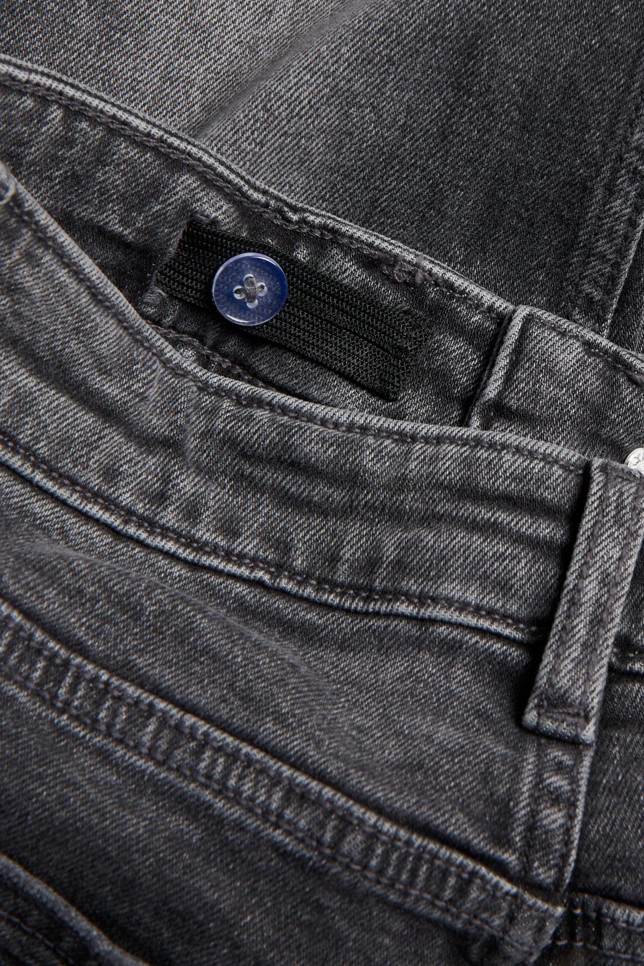 Närbild på barnens raka jeans i grå denim med medelhög midja, justerbar resår och blå knapp.