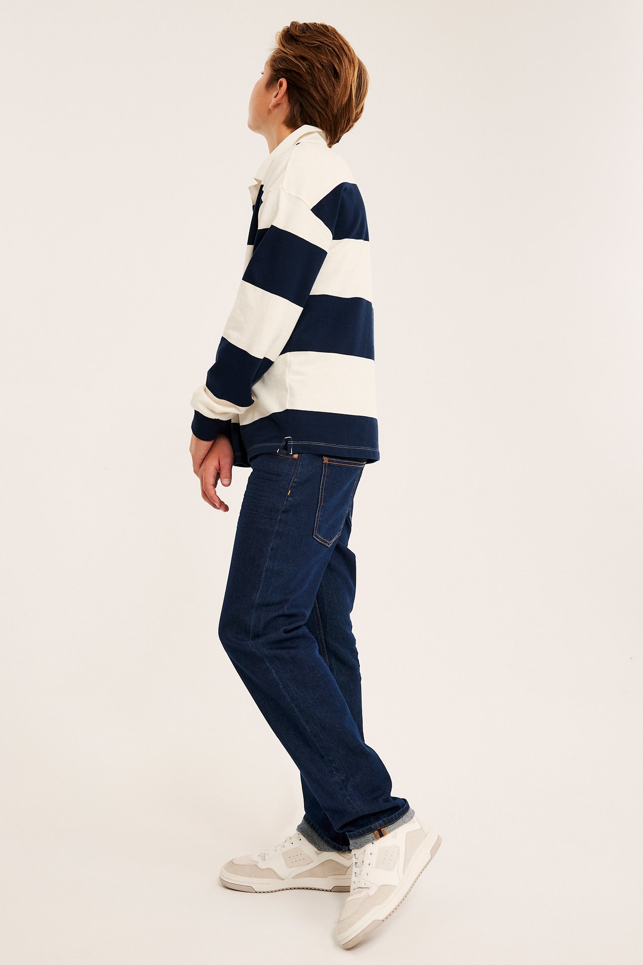 Barn iført marineblå og hvit stripete langermet rugbyskjorte, mørkeblå jeans og lyse joggesko.