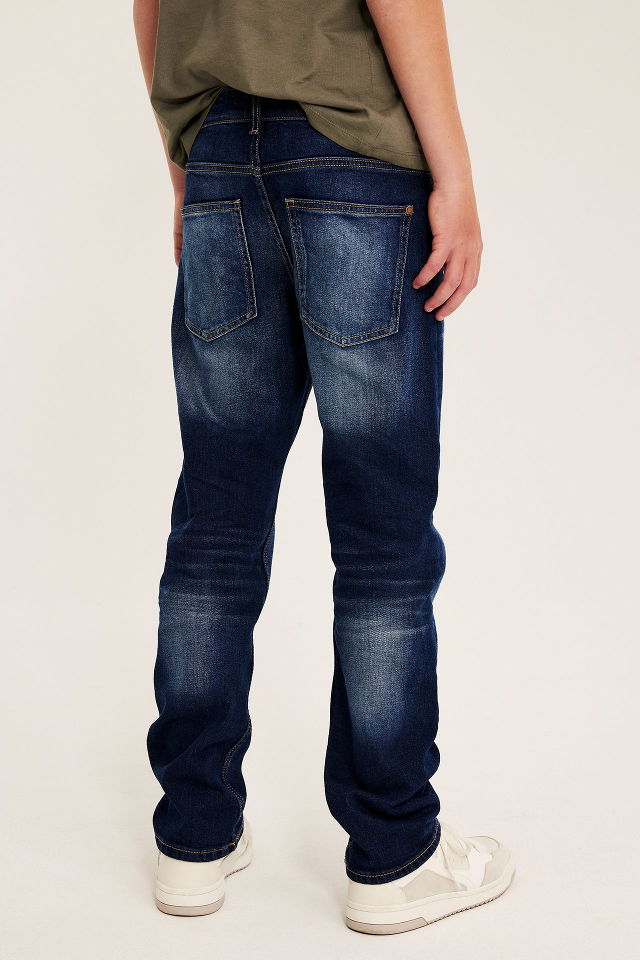 Barn bakifrån i mörkblå raka jeans, en grön t-shirt och vita sneakers.