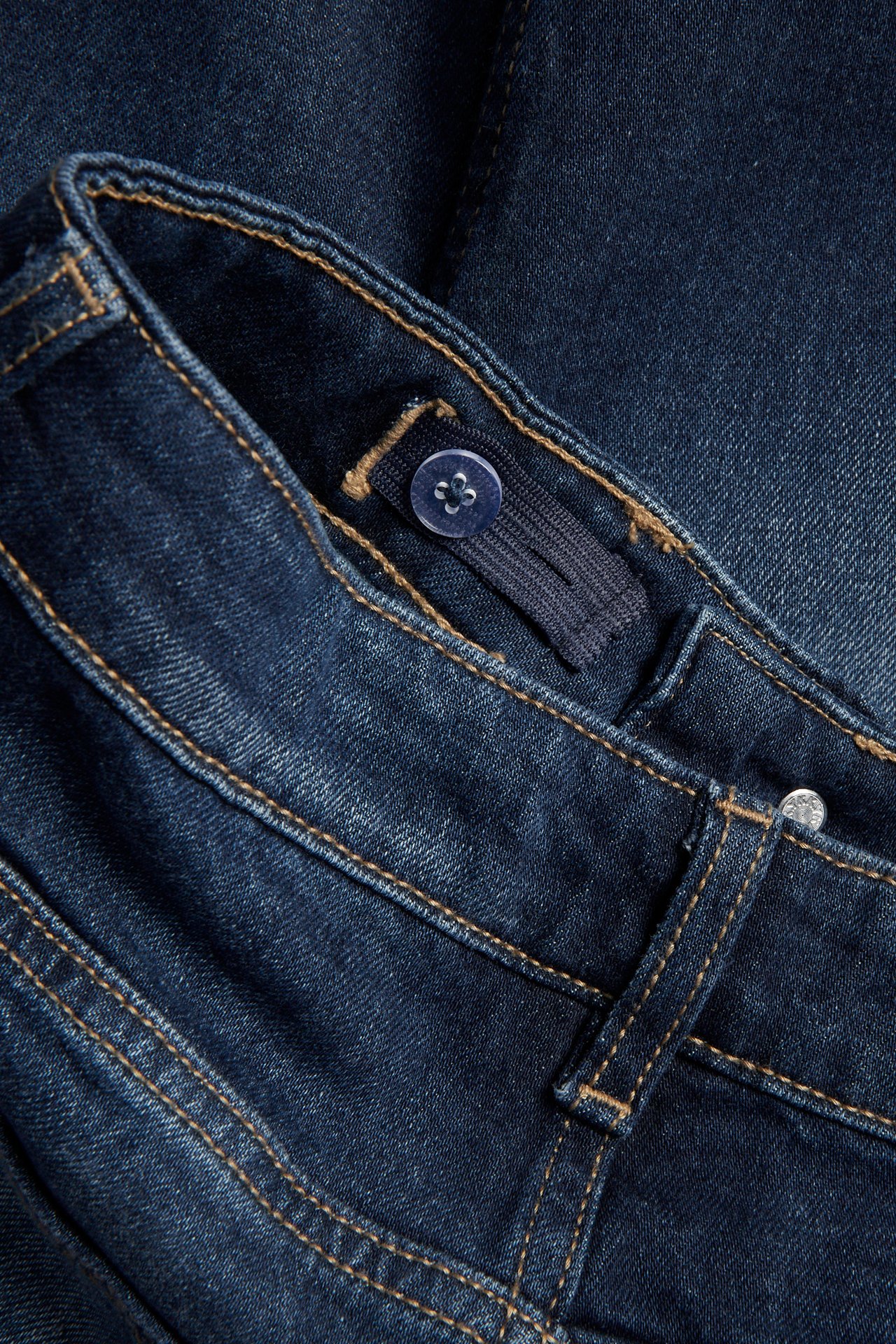 Närbild av mörkblå raka denimjeans med justerbar resår och knapp inuti midjebandet.