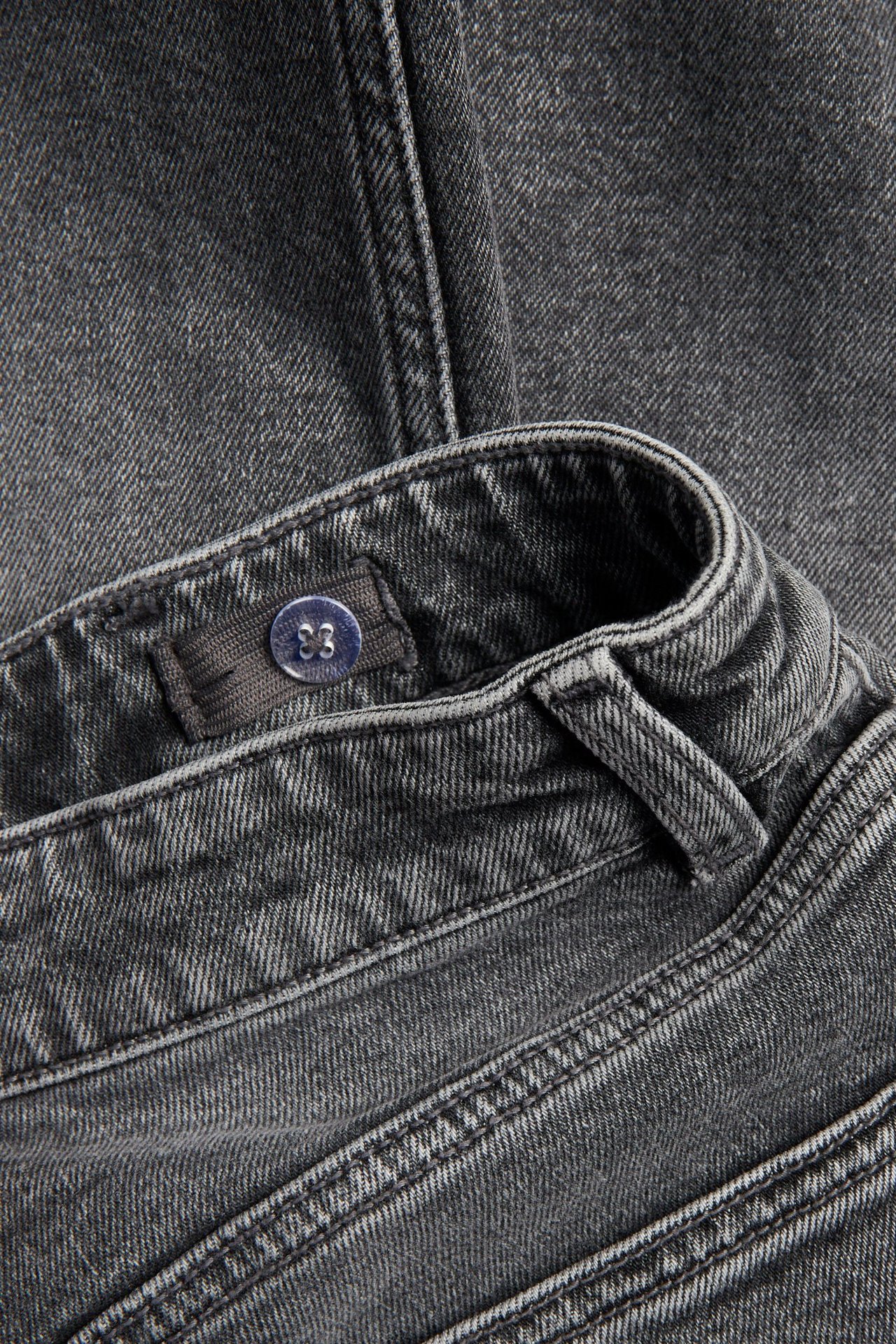 Lähikuva harmaista denim-väljistä mid-waist farkuista, joissa näkyy säädettävä nappivyötärö.