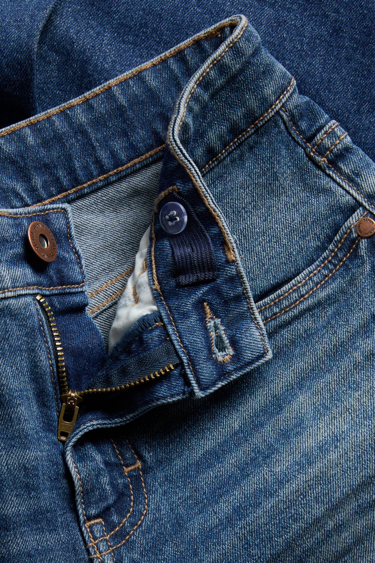 Närbild av blåa lösa denimjeans med medelhög midja, öppen gylf, metallknapp och justerbar resår i midjan.