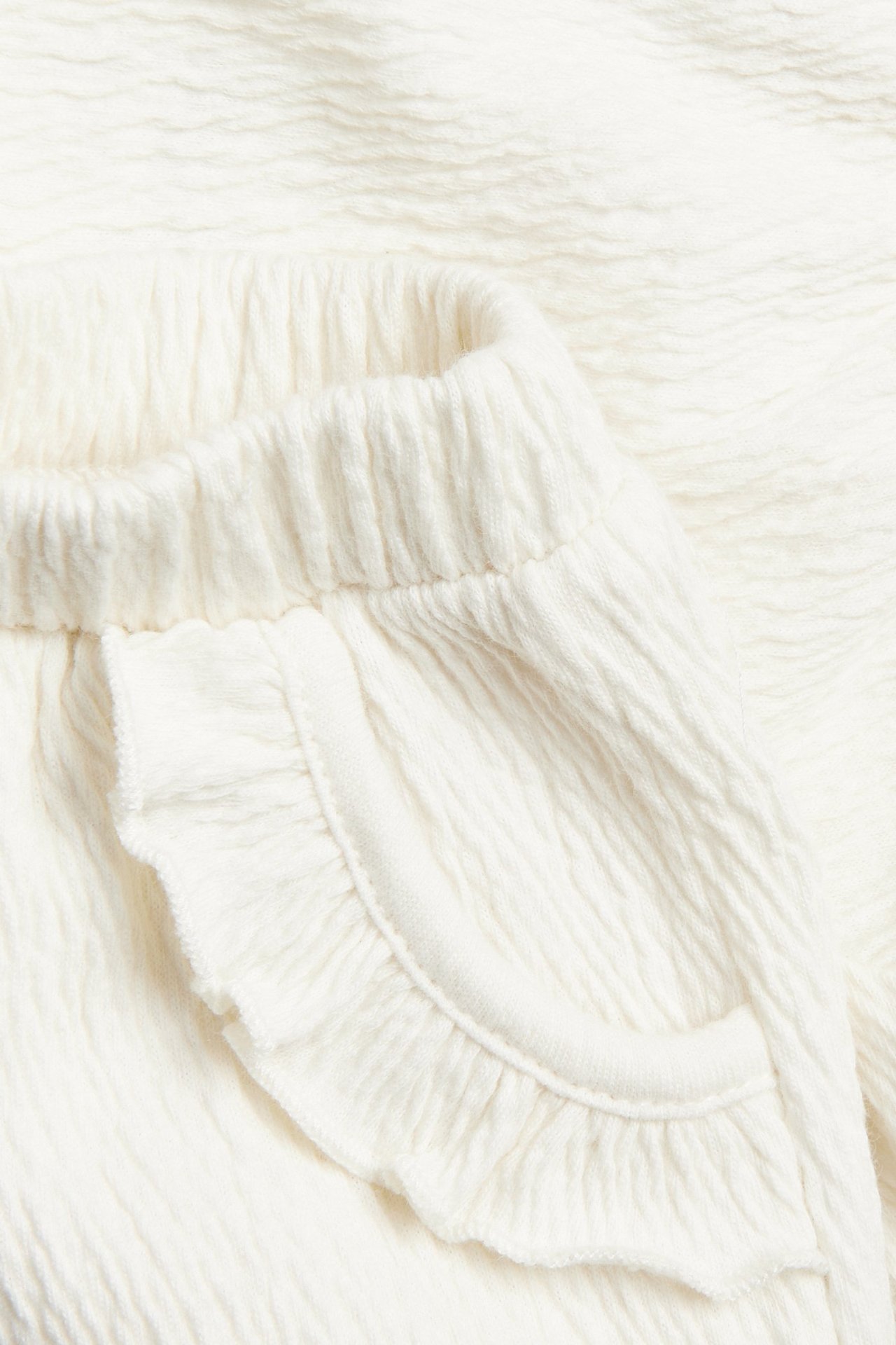 Zbliżenie na kremowe marszczone szorty niemowlęce z elastyczną talią i falbankami przy kieszeniach.