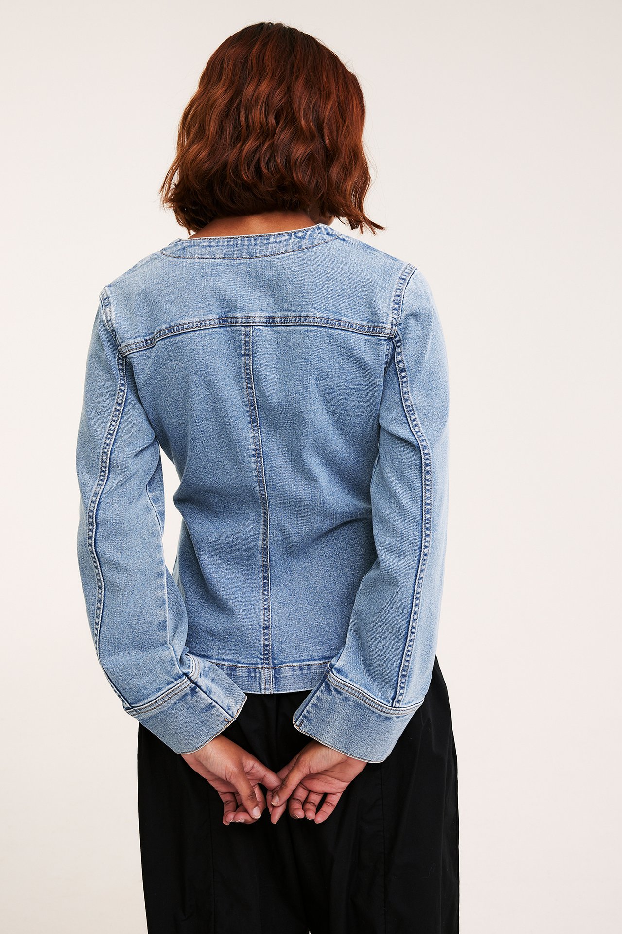 Takakuva naisesta yllään vaalea, vartalonmyötäinen denim-puserojakku ja mustat housut.