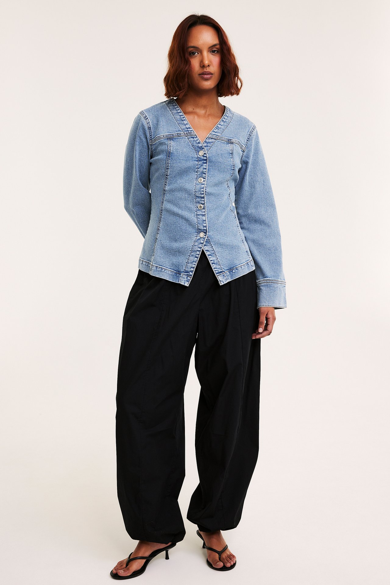 Edestä, nainen yllään vaaleansininen istuva farkkublousitakki napeilla, mustat leveät housut ja mustat sandaalit.