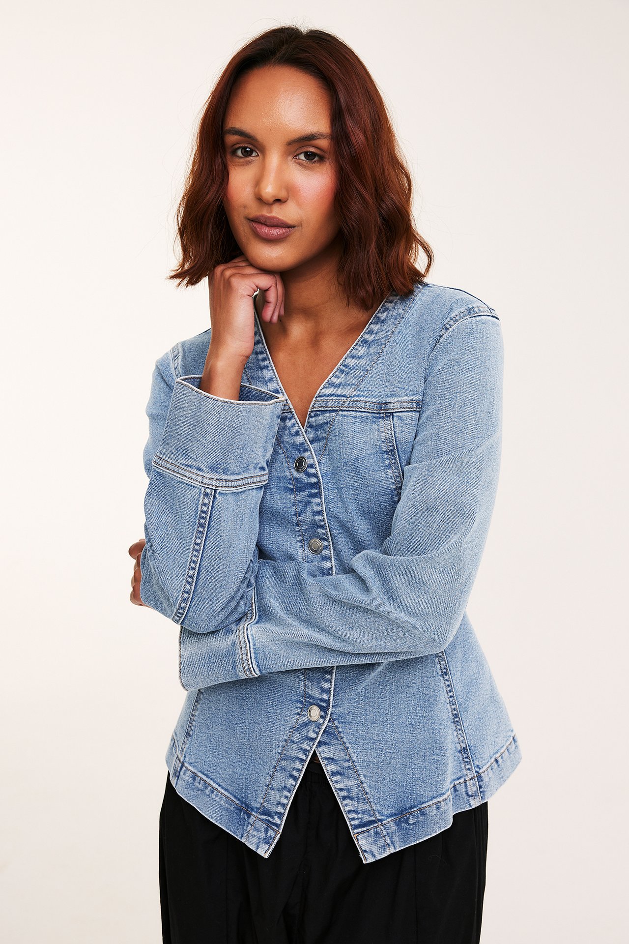 Edestä: Nainen yllään istuva vaalea denimitakki V-pääntiellä, napeilla ja mustilla housuilla.