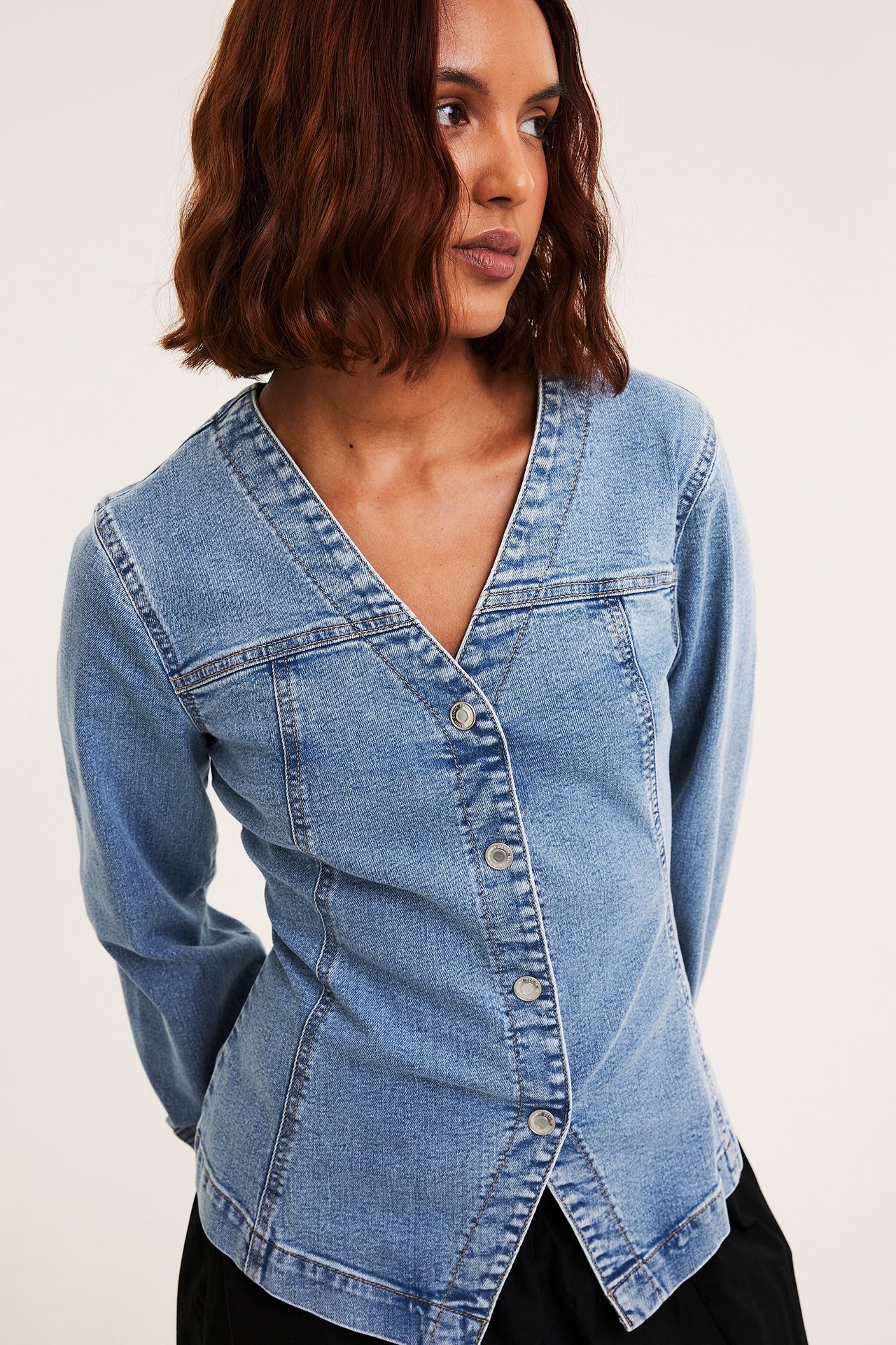 Frontbilde av kvinne i lys blå figursydd stretch-denimblusejakke med sølvfargede knapper.
