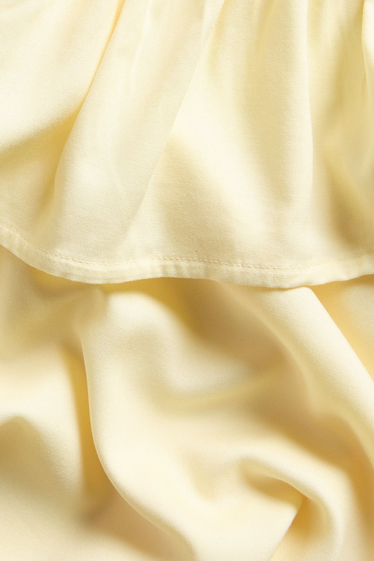 Zbliżenie na jasnożółtą jednobarwną sukienkę z wiskozy na jedno ramię z falbaną.