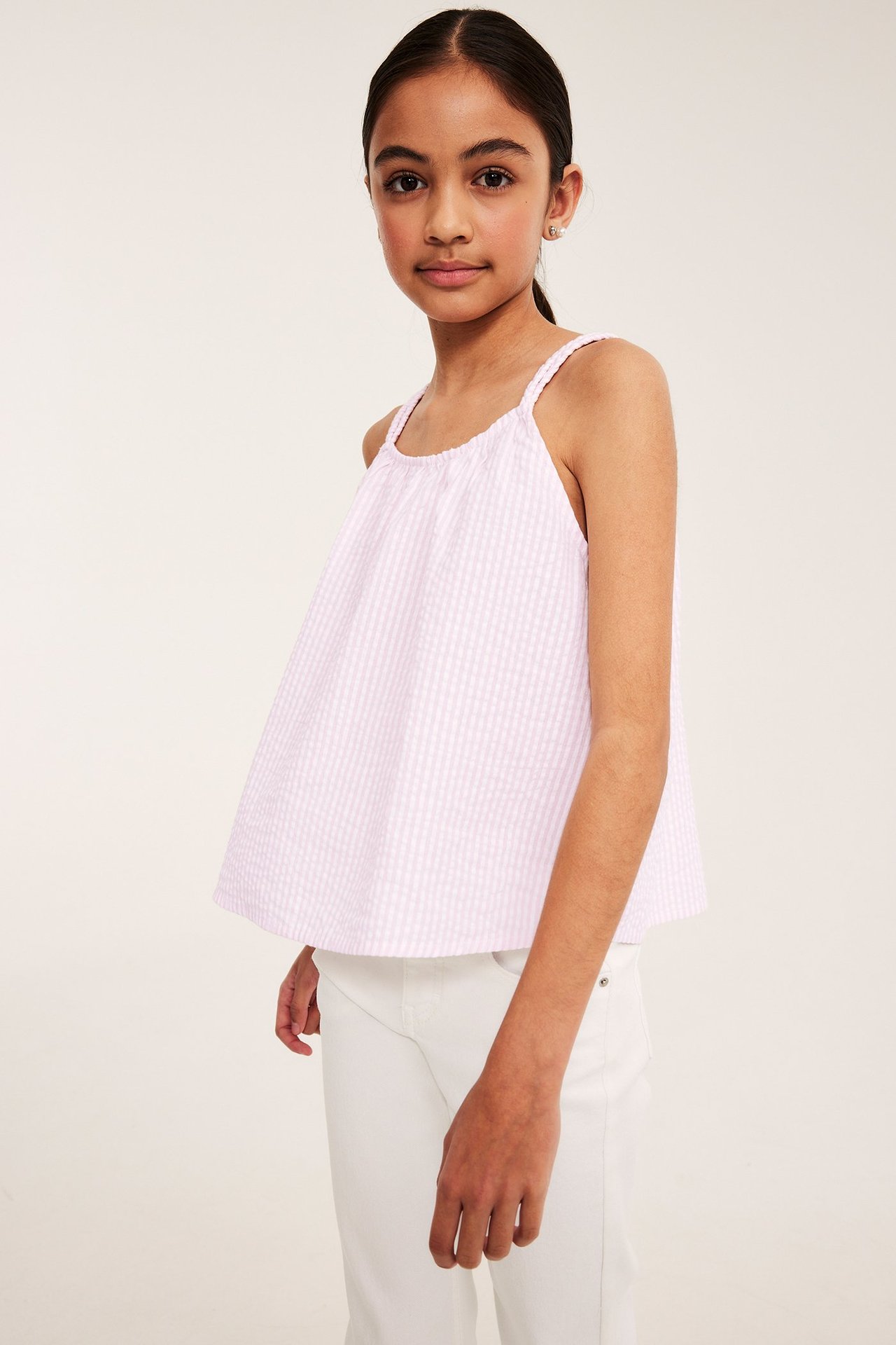 Lapsi yllään väljä vaaleanpunainen raidallinen seersucker-toppi punotuilla olkaimilla ja valkoiset housut.