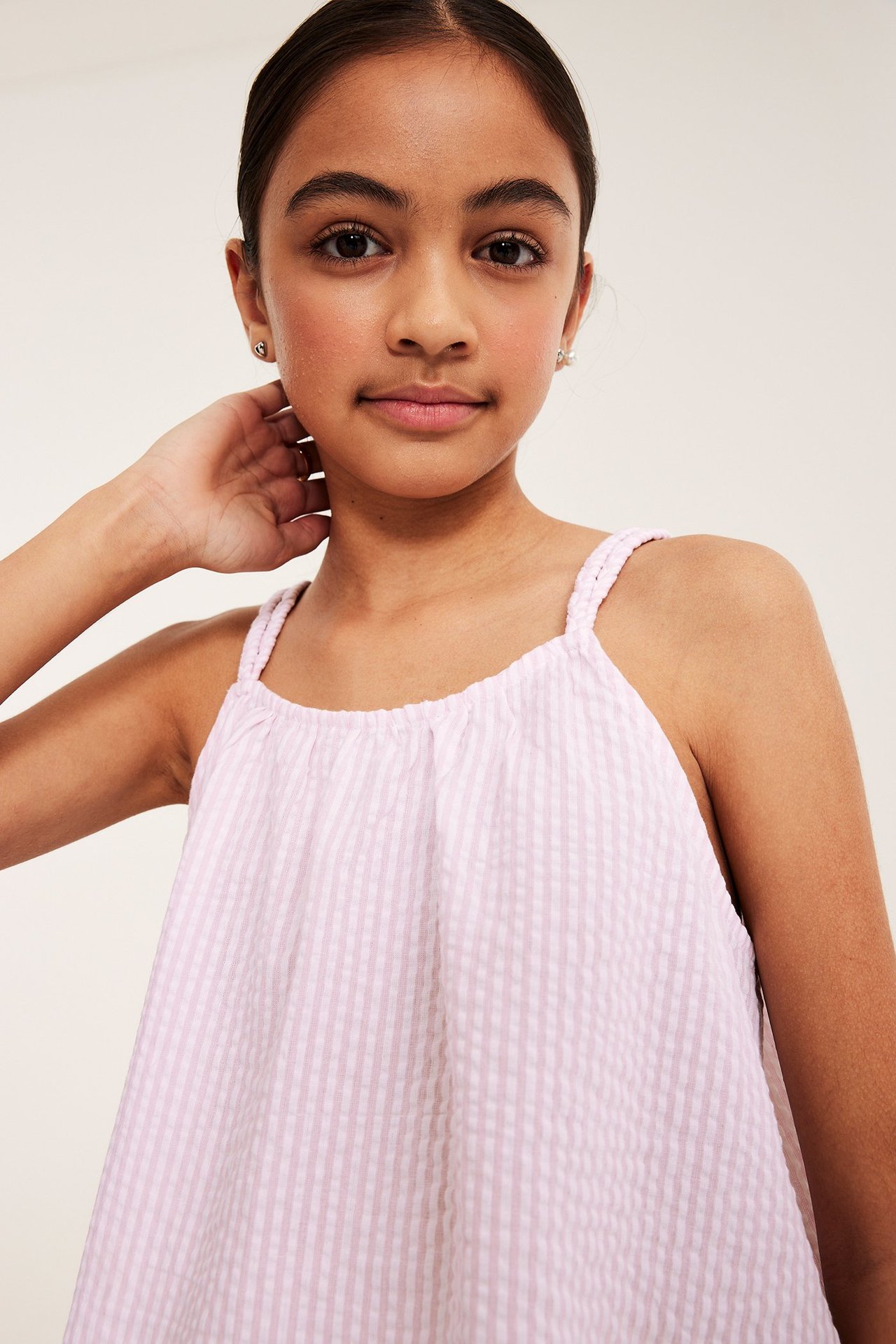 Framifrån, ett barn i en rosa randig bäckebölja-topp med flätade axelband.