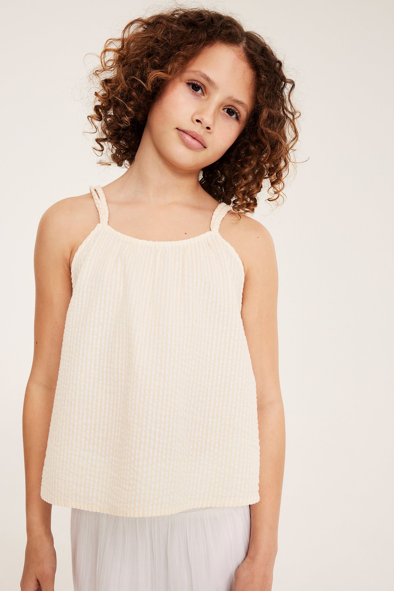 Widok z przodu: Dziecko w żółtym, paskowym topie z seersuckeru z plecionymi ramiączkami i szarej spódnicy.