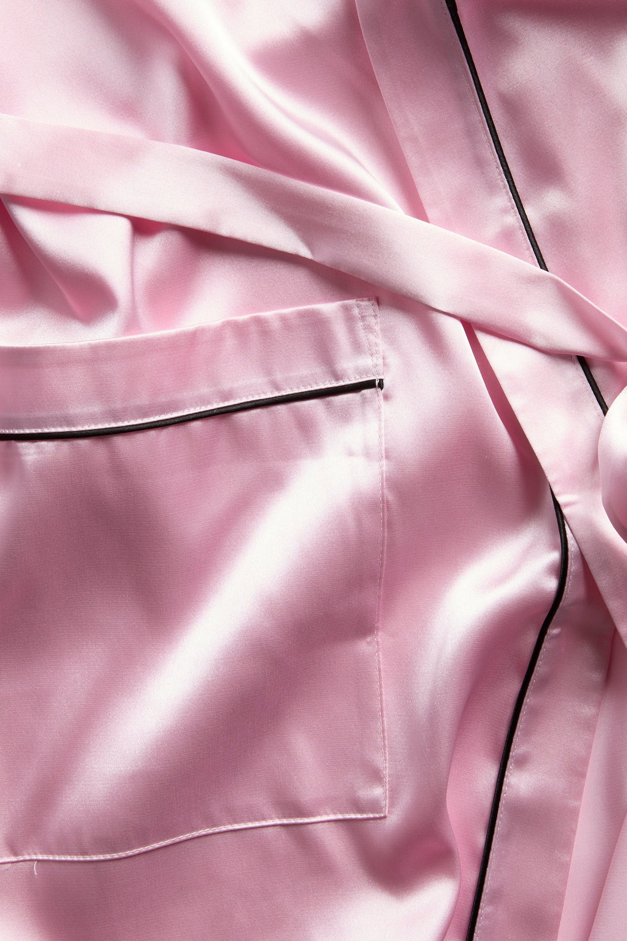 Närbild på rosa satinrock eller pyjamas med svarta passpoaldetaljer och en ficka.