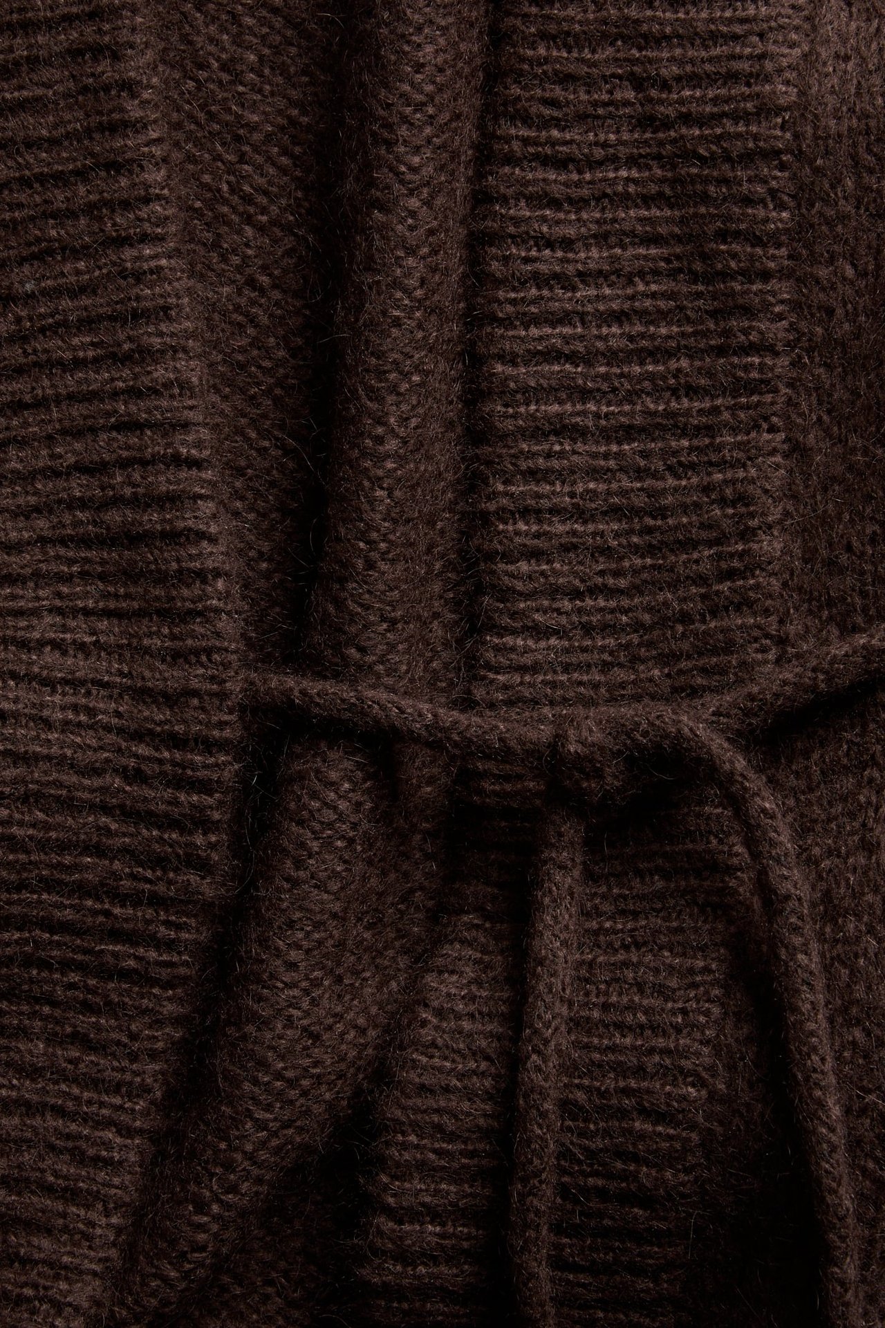 Lähikuva ruskeasta villasekoitepitkästä neuletakista, jossa näkyvä solmuyksityiskohta ja neulottu pinta.